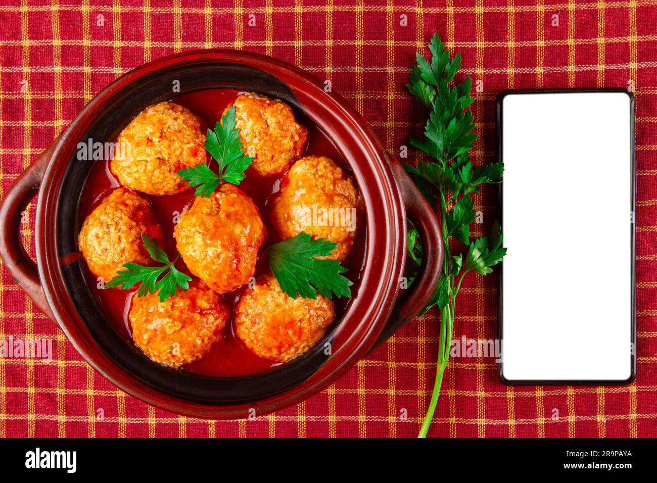 Polpette di pollo in salsa di pomodoro e smartphone con schermo bianco Foto Stock