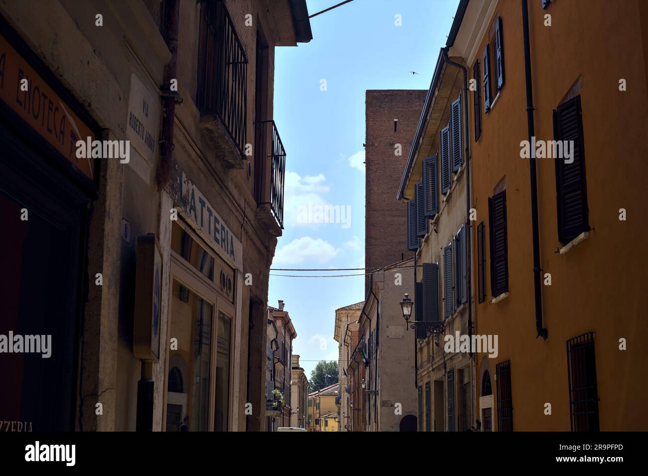 La strada è circondata da alti edifici e da una torre lontano in una giornata di sole in una città italiana Foto Stock