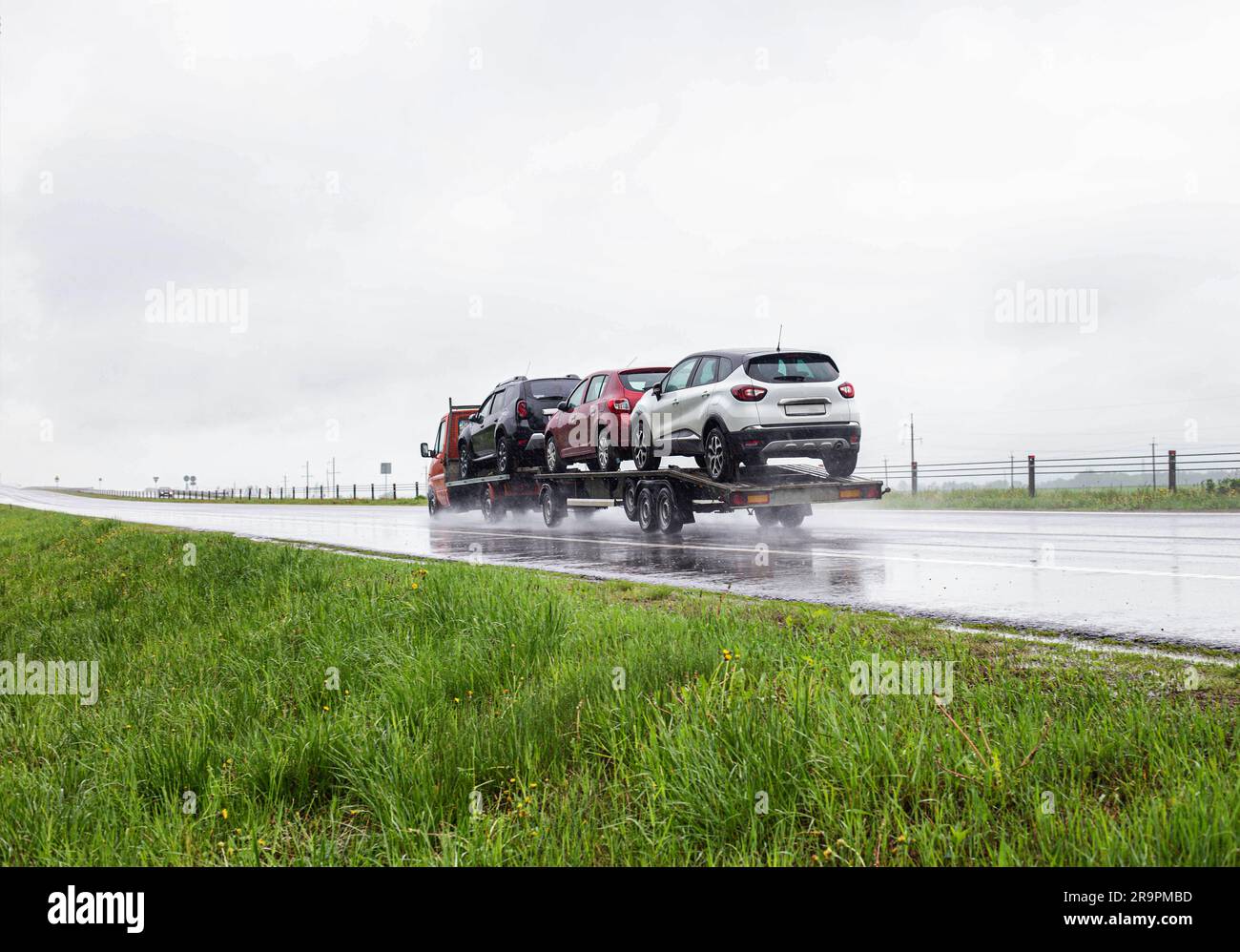 Un autotrasportatore con rimorchio trasporta le auto in condizioni di pioggia torbida su un'autostrada scivolosa. Servizi di trasporto auto, affari. Foto Stock