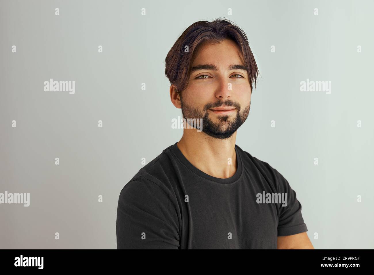 Ritratto di un bel giovane sorridente con le braccia piegate. Uomo sorridente e gioioso con le mani incrociate ripresa in studio. Isolato su sfondo grigio. Ritratto di y Foto Stock