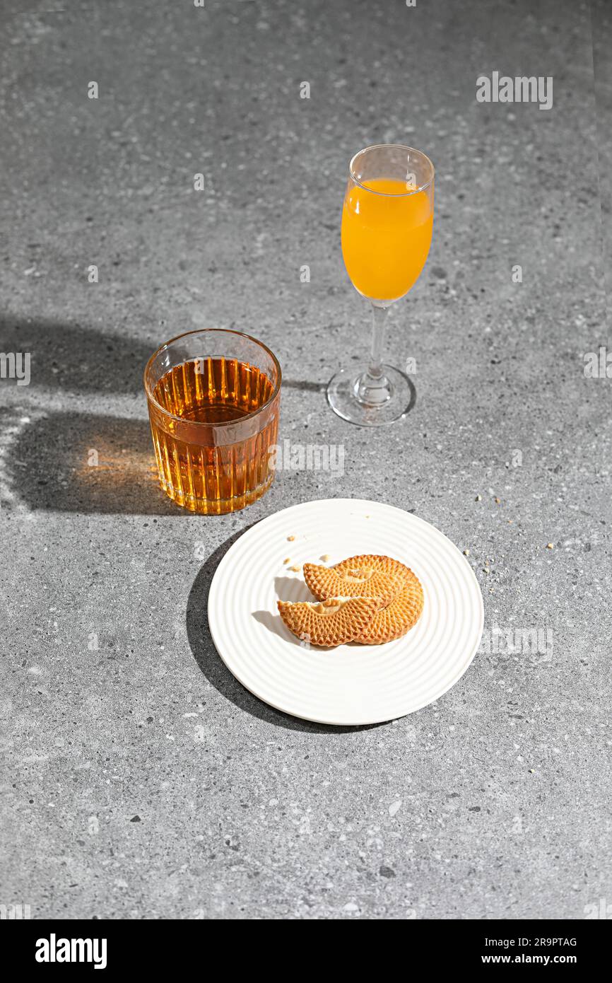 Un piatto bianco con biscotti appena sfornati su una superficie grigia di cemento, con due bicchieri di colorate bevande rinfrescanti Foto Stock