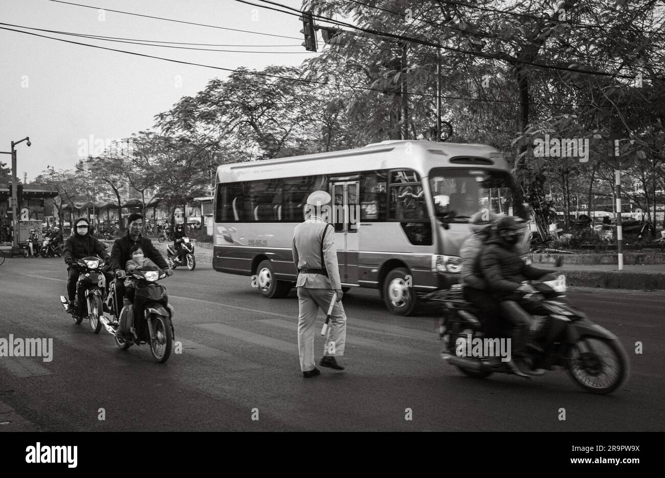 Un poliziotto attraversa Yen Phu Road tra le motociclette e un autobus ad Hanoi, in Vietnam. Foto Stock