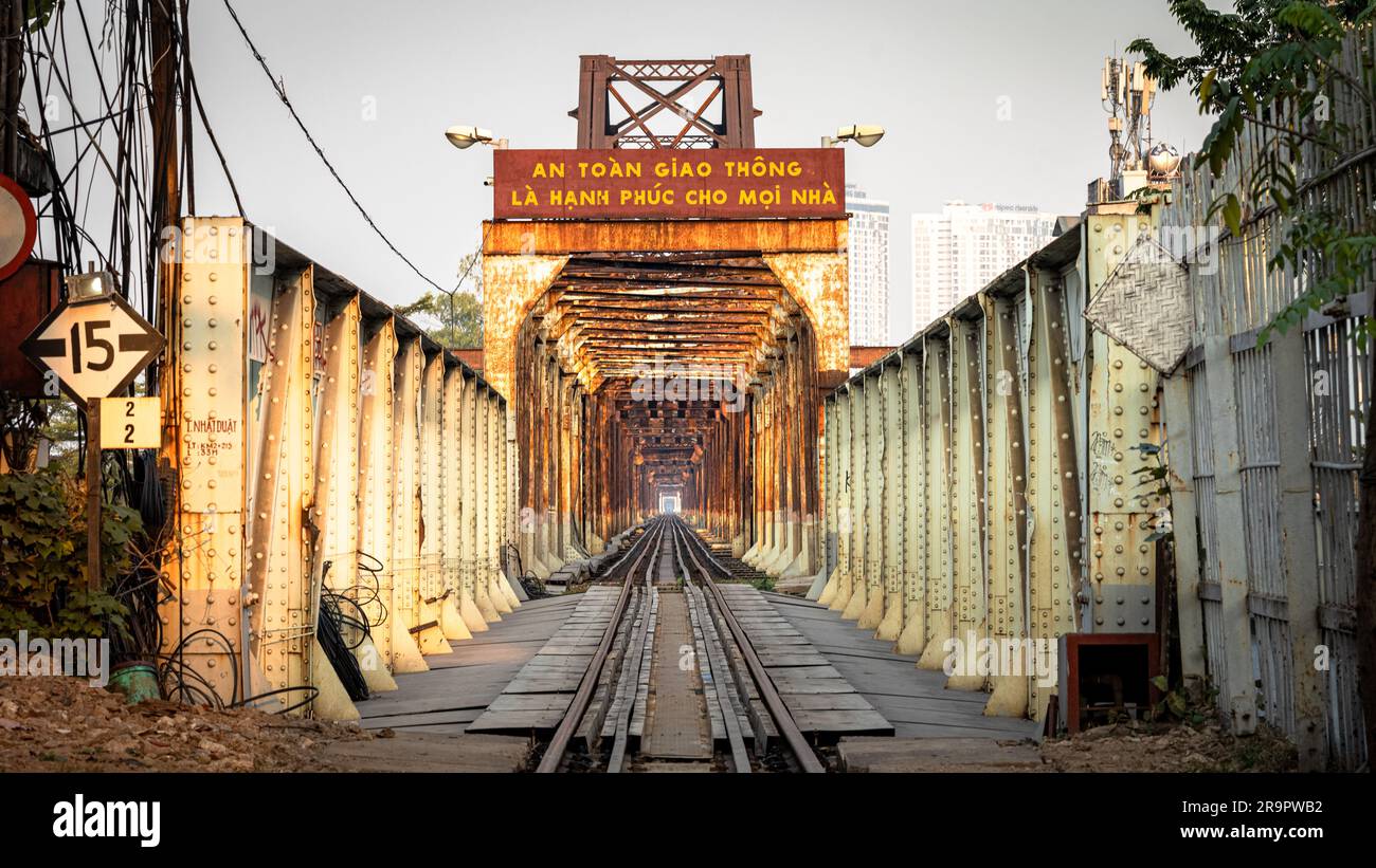 Una vista lungo i binari ferroviari attraverso il ponte arrugginito Long Bien ad Hanoi, Vietnam. Il cartello recita: La sicurezza stradale è la felicità di ogni casa Foto Stock
