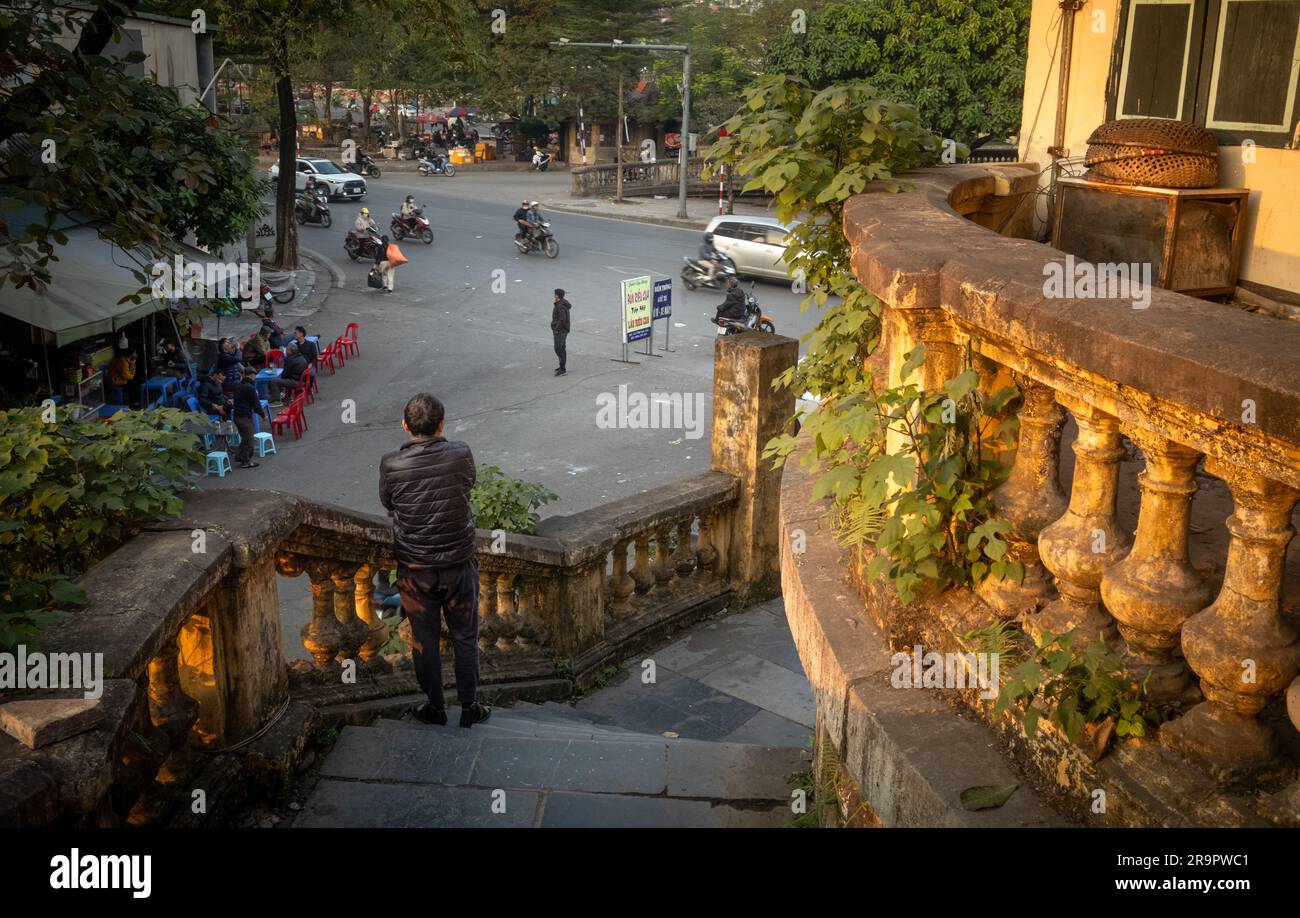 Un uomo vietnamita sorge su gradini dell'epoca coloniale francese che conducono alla stazione ferroviaria di Long Bien, affacciata su Yen Phu Road ad Hanoi, Vietnam. Foto Stock