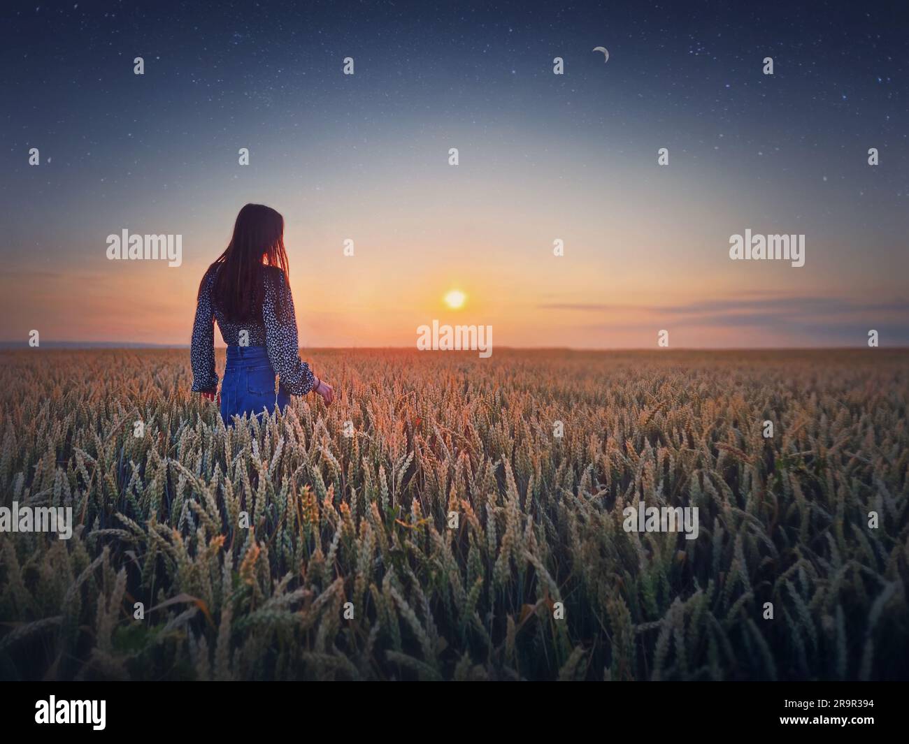 Giovane donna nel campo di grano dorato al tramonto. Splendido scenario al crepuscolo sotto il sole estivo e la luna a mezzaluna con cielo stellato Foto Stock