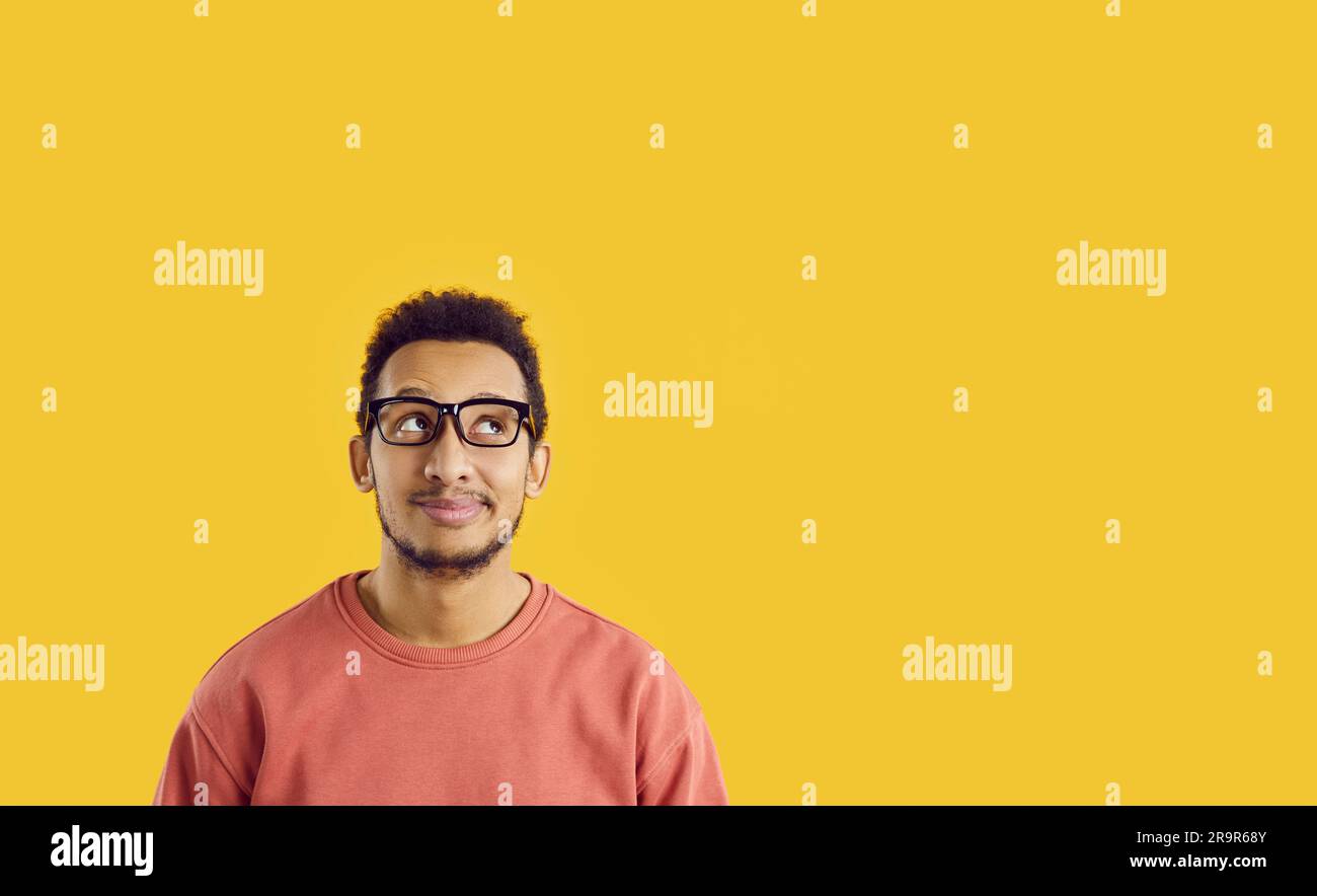 Sorridente e sognante ragazzo afro-americano immagina qualcosa di bello su sfondo giallo brillante. Foto Stock