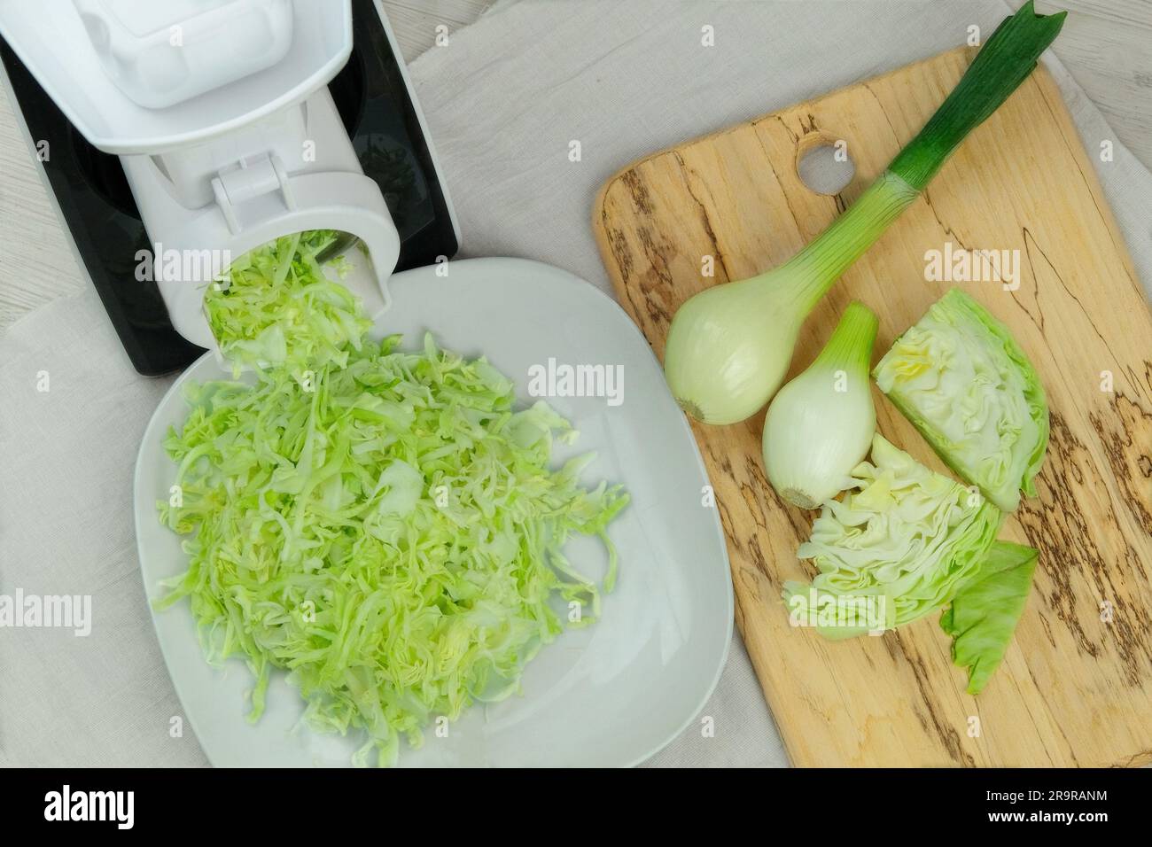 Cavolo in una taglierina per verdure sul tavolo da cucina. Il cavolo tritato sta cadendo in una ciotola. Cibo sano fatto in casa. Foto Stock