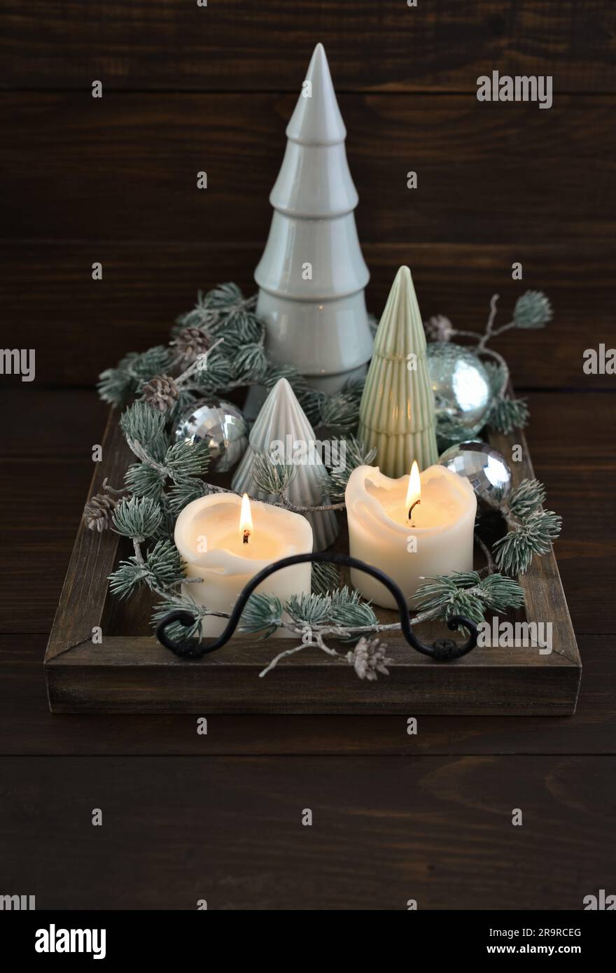 Abeti decorativi in ceramica con palline di natale blu e candele su vassoio di legno su sfondo di legno scuro Foto Stock