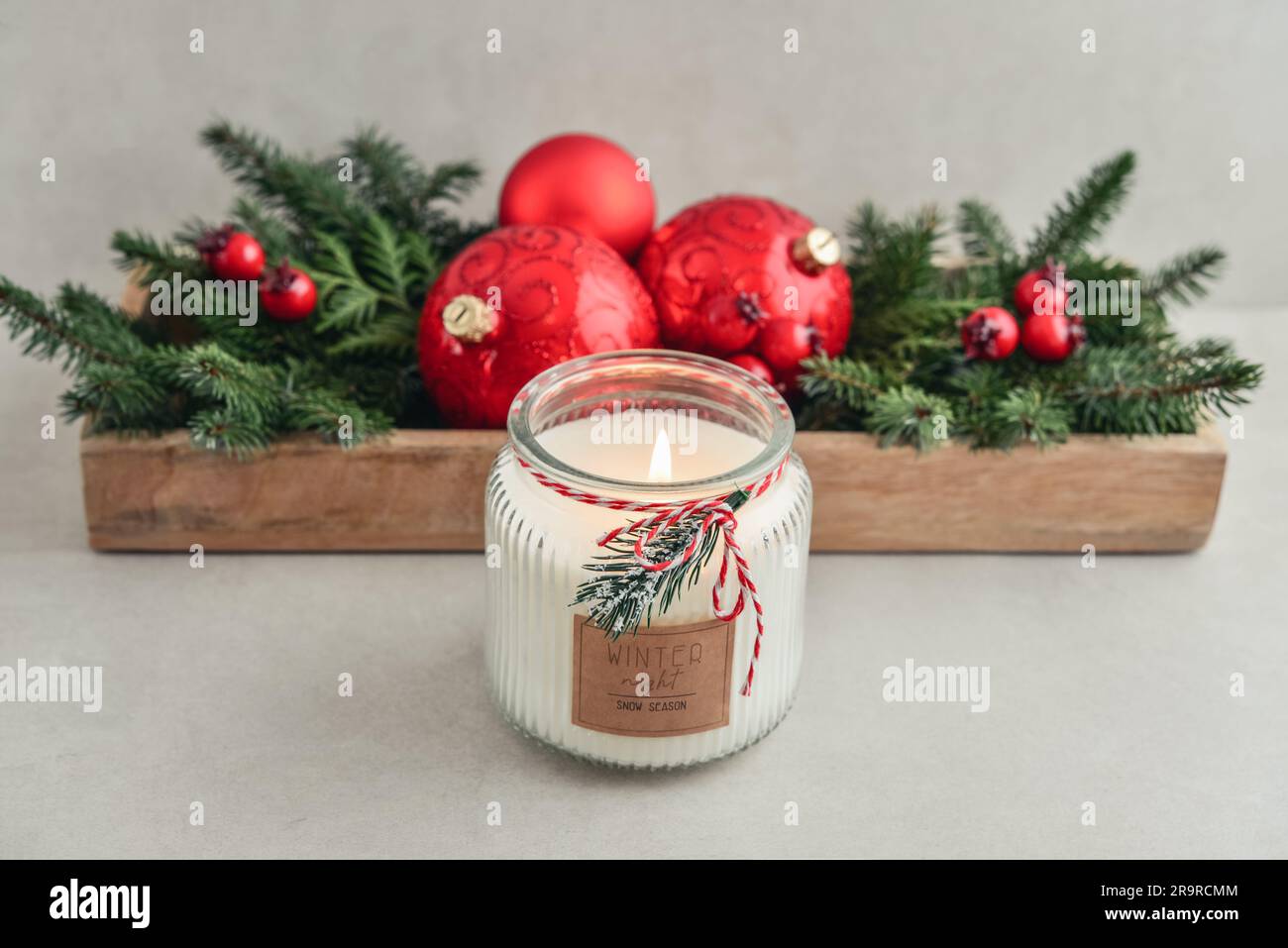 Candela in vaso con decorazioni natalizie dai rami degli abeti e palline di natale rosse su sfondo chiaro Foto Stock