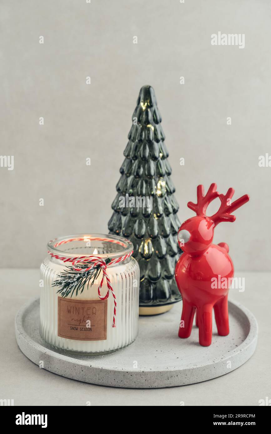 Abete decorativo in vetro con cervo in ceramica rossa e candela in vaso su vassoio di pietra su sfondo chiaro Foto Stock