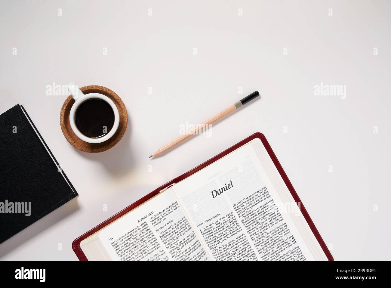 Lastra piatta della Bibbia cristiana aperta al Libro di Daniele con caffè espresso, taccuino e matita su sfondo bianco foto di scorta Foto Stock
