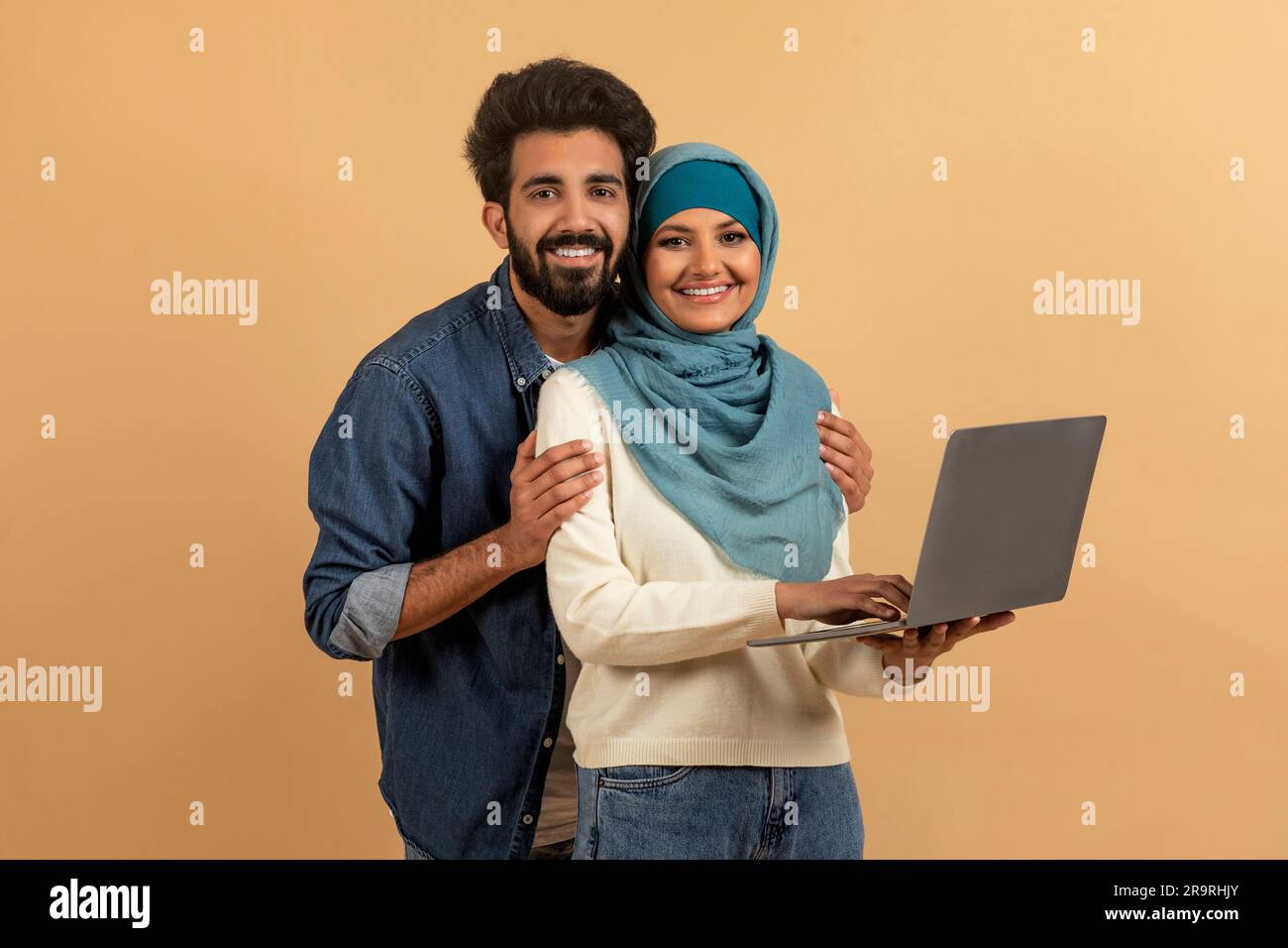 Felice giovane coppia musulmana con un notebook in mano in posa su sfondo beige Foto Stock