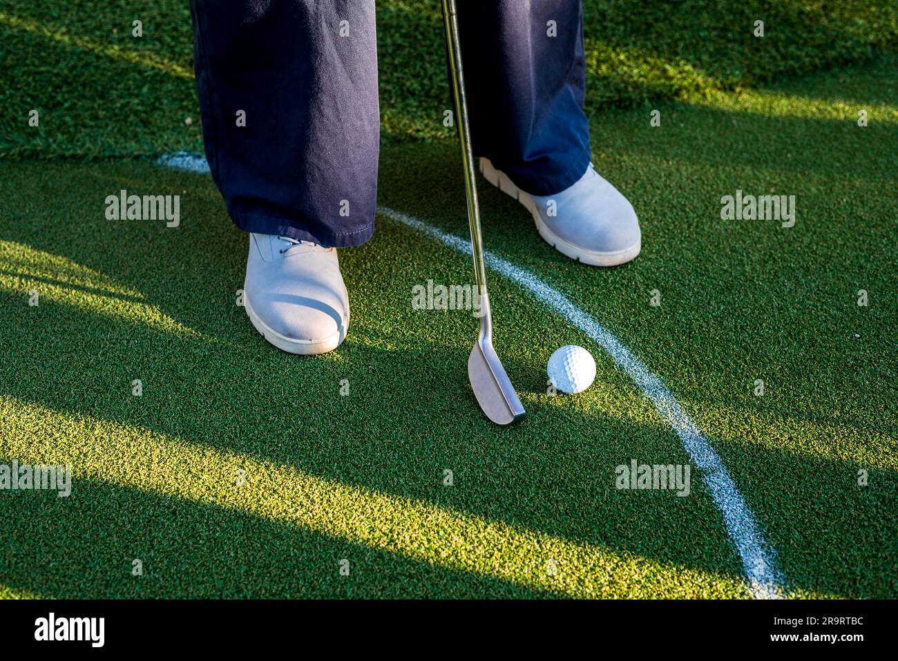 Giocatore di minigolf con scarpe da ginnastica grigie che mette la palla nella buca sulla corsia verde. Foto Stock