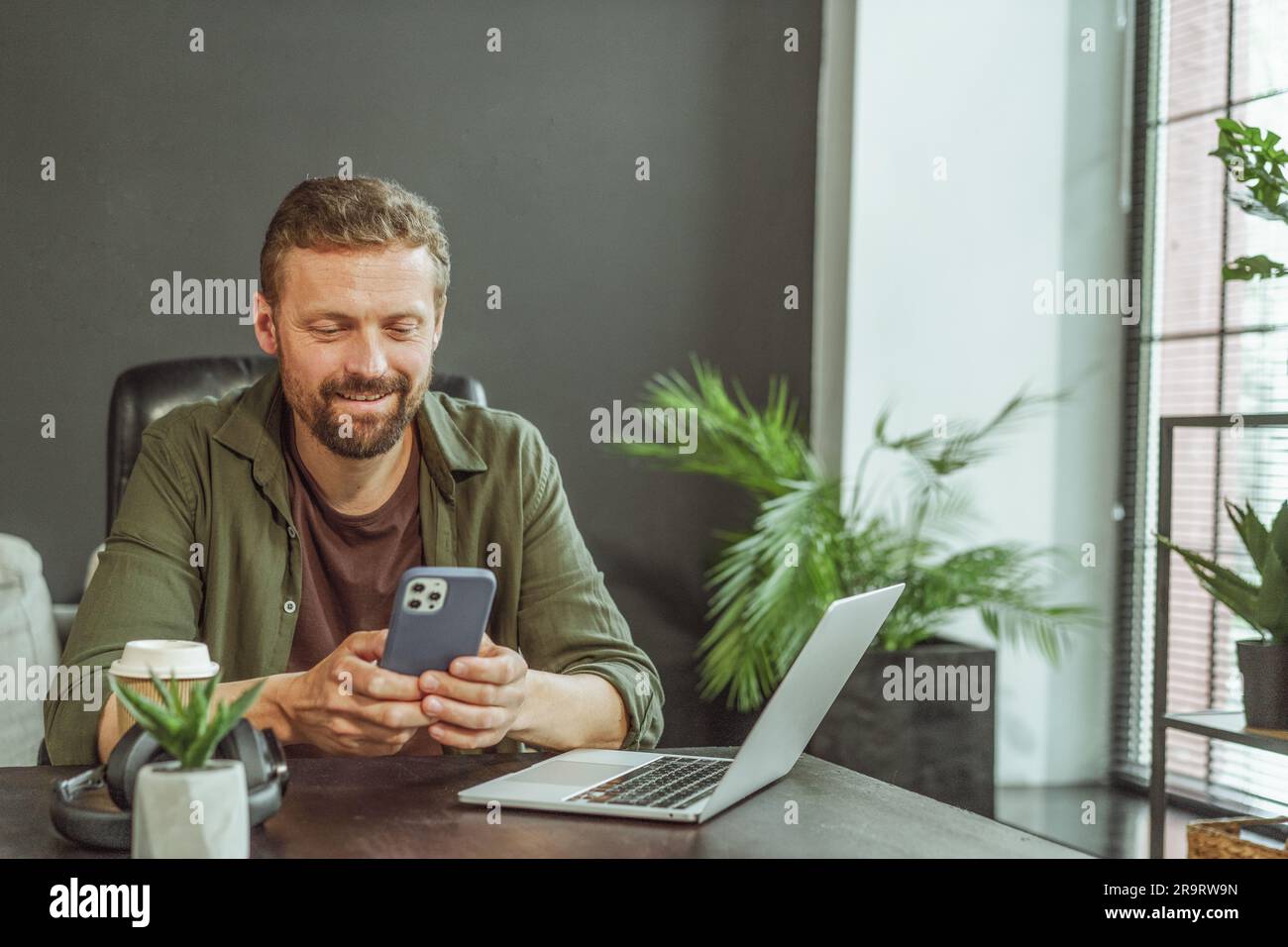 Un momento in ufficio dove un uomo si sta prendendo una pausa dal lavoro al computer. È stato visto inviare un messaggio di testo sul suo telefono, che mostra la natura multitasking degli ambienti di lavoro moderni. Foto di alta qualità Foto Stock