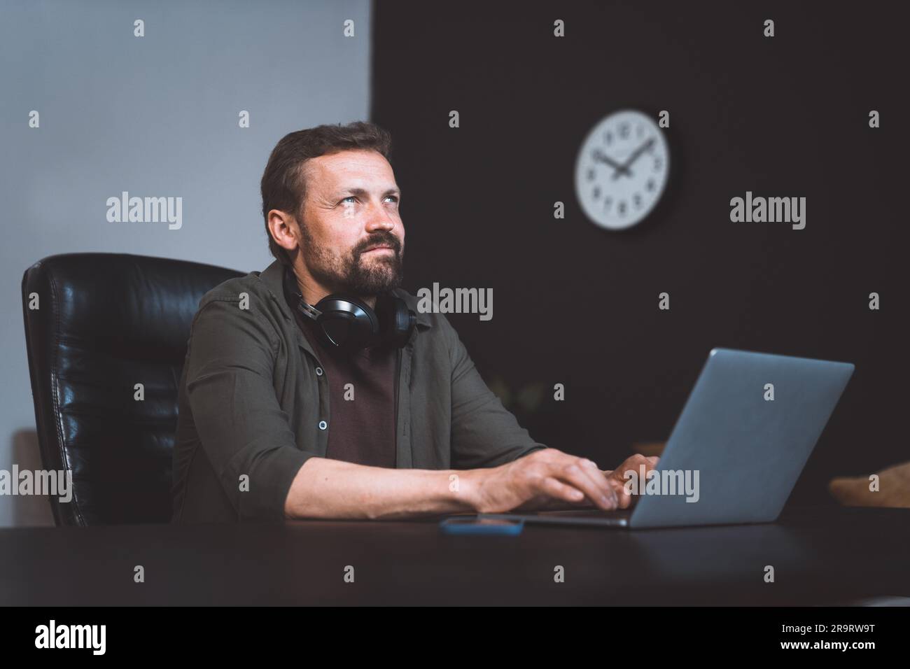 Lavoratore che sogna ad occhi aperti mentre è seduto in ufficio. Uomo vestito in stile casual, che digita un notebook. Tuttavia, lo sguardo lontano e la postura rilassata suggeriscono che ha perso nei pensieri, indulgendo nel momento di sognare. Foto di alta qualità Foto Stock