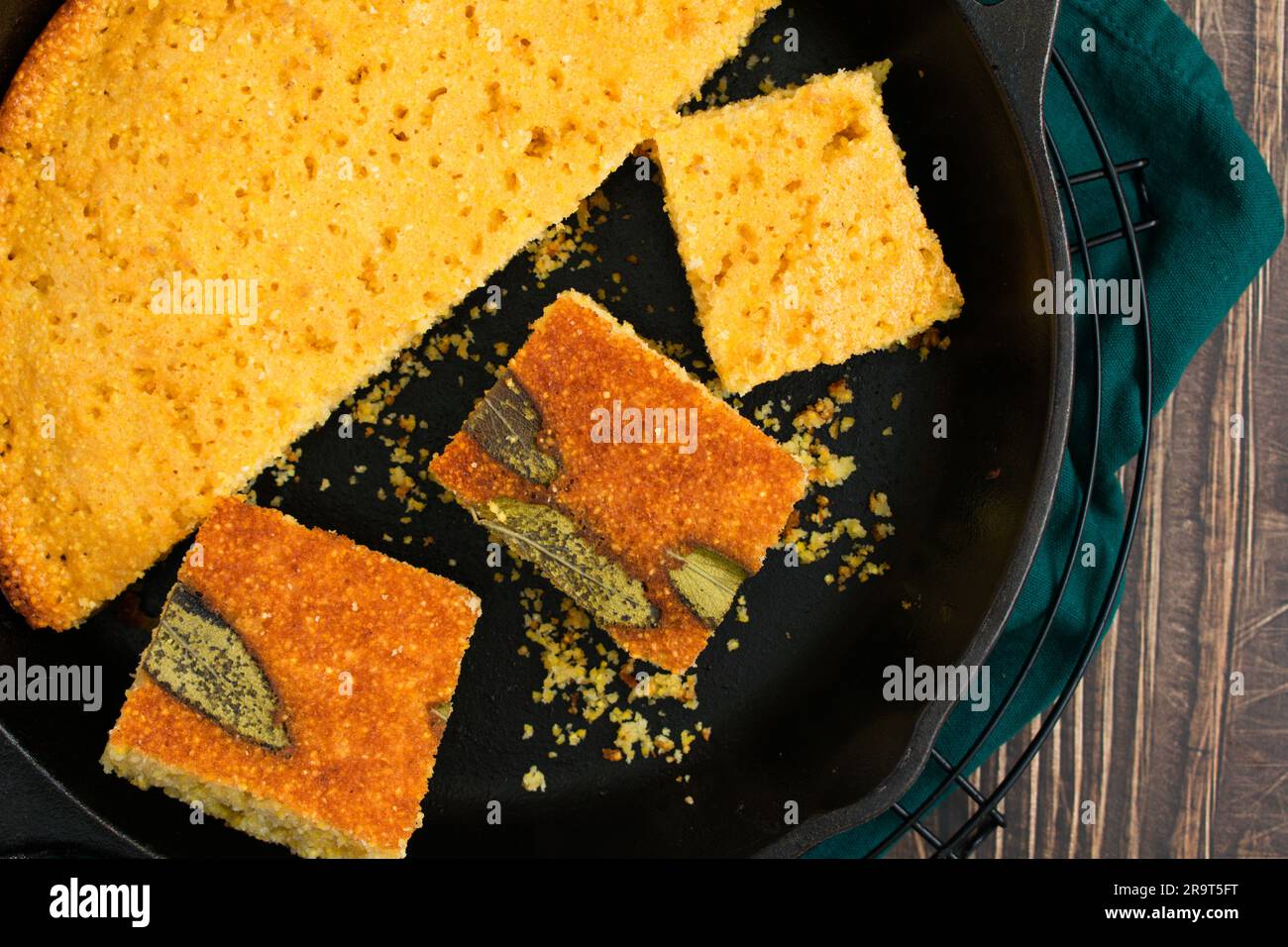 Pane di mais salvia tagliato a pezzetti in un pezzetto di ghisa: Pane di mais al burro del sud appena sfornato in una padella con burro e miele a lato Foto Stock