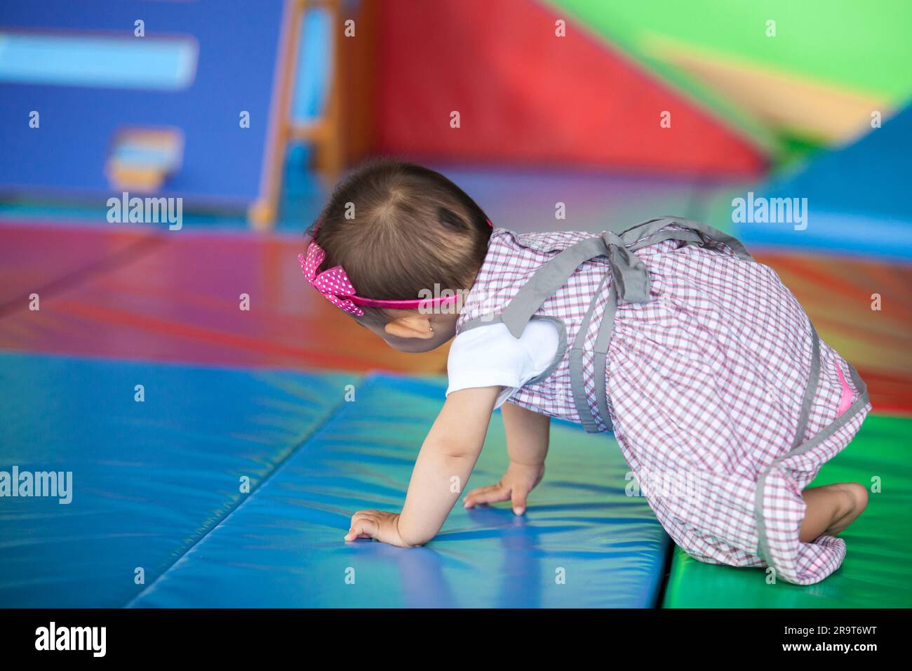 Bella bambina di dieci mesi che strisciava su uno sfondo colorato. Concetto di stimolazione precoce per i bambini piccoli. Foto Stock