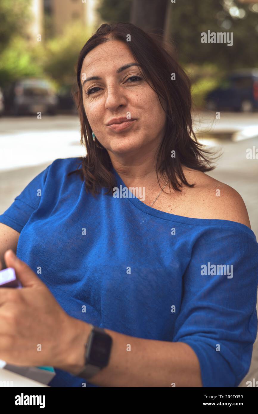 Ritratto di una donna bruna in un bar, indossando un maglione blu e godendosi l'ambiente esterno. Foto Stock