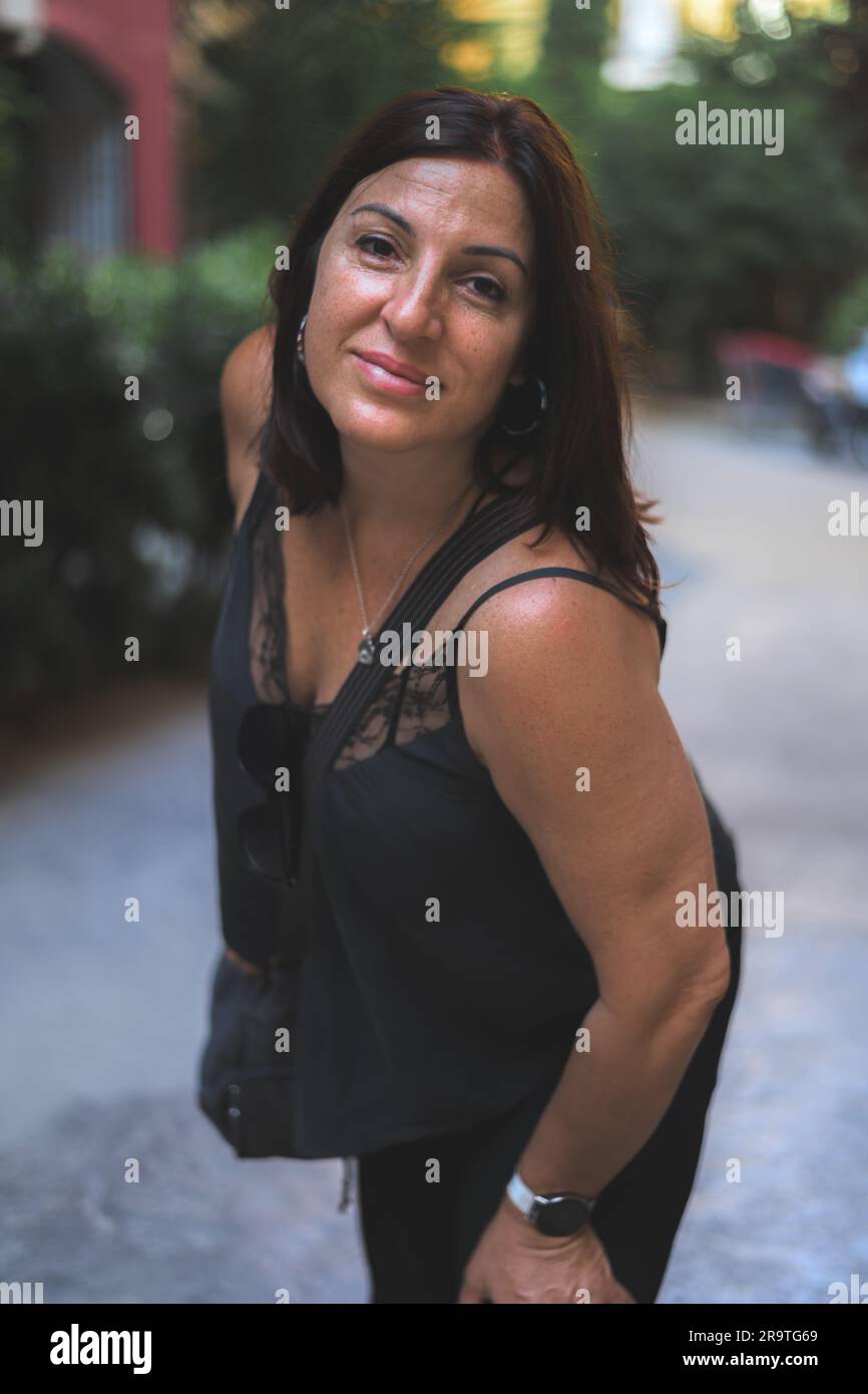 Una foto a mezzo busto di una bruna all'aperto, vestita di abiti neri, appoggiata verso la fotocamera. Foto Stock