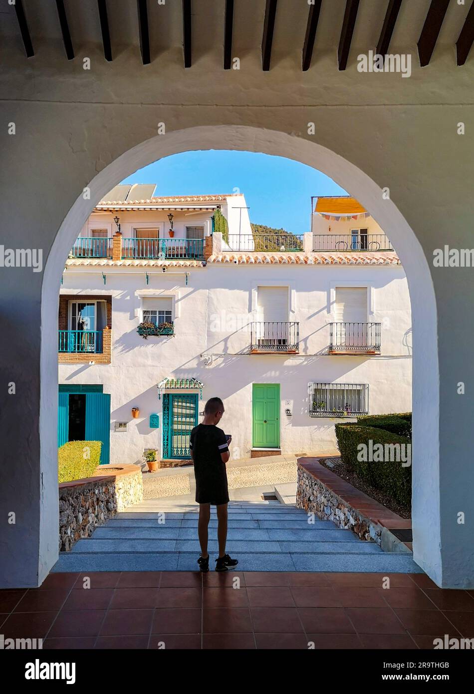 Ragazzo che controlla il telefono sotto Arch nel villaggio bianco di Frigiliana, provincia di Malaga, Andalusia, Spagna Foto Stock