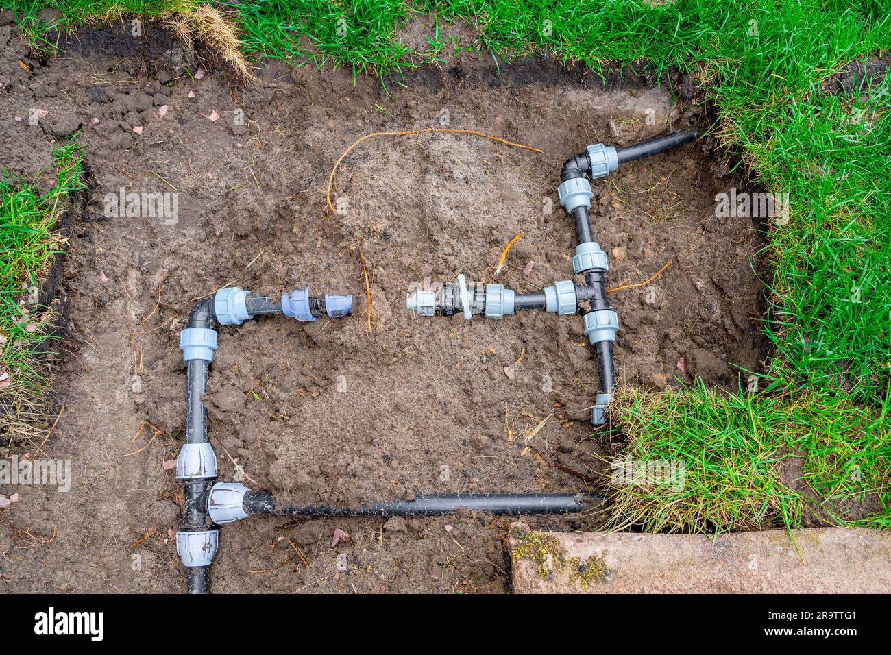 Tubi in plastica e cablaggio del circuito per l'irrigazione del prato. Raccordi di collegamento e valvole per la chiusura dell'acqua in giardino Foto Stock