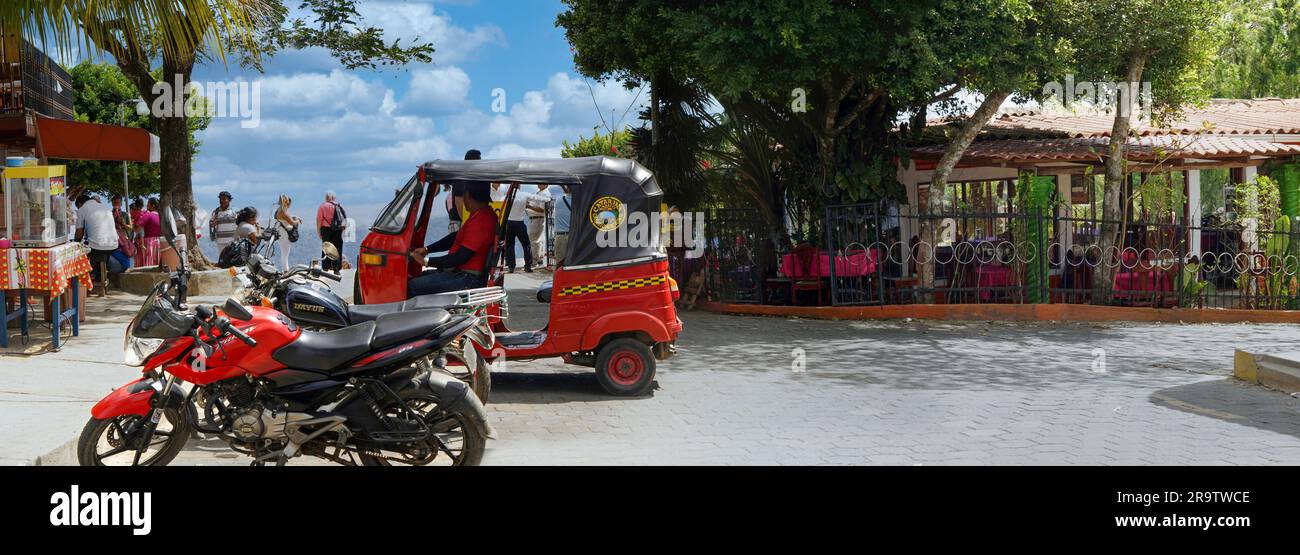 Jinrikisha e motociclette in strada nel villaggio di Catarina con Laguna de Apoyo sullo sfondo, Nicaragua Foto Stock