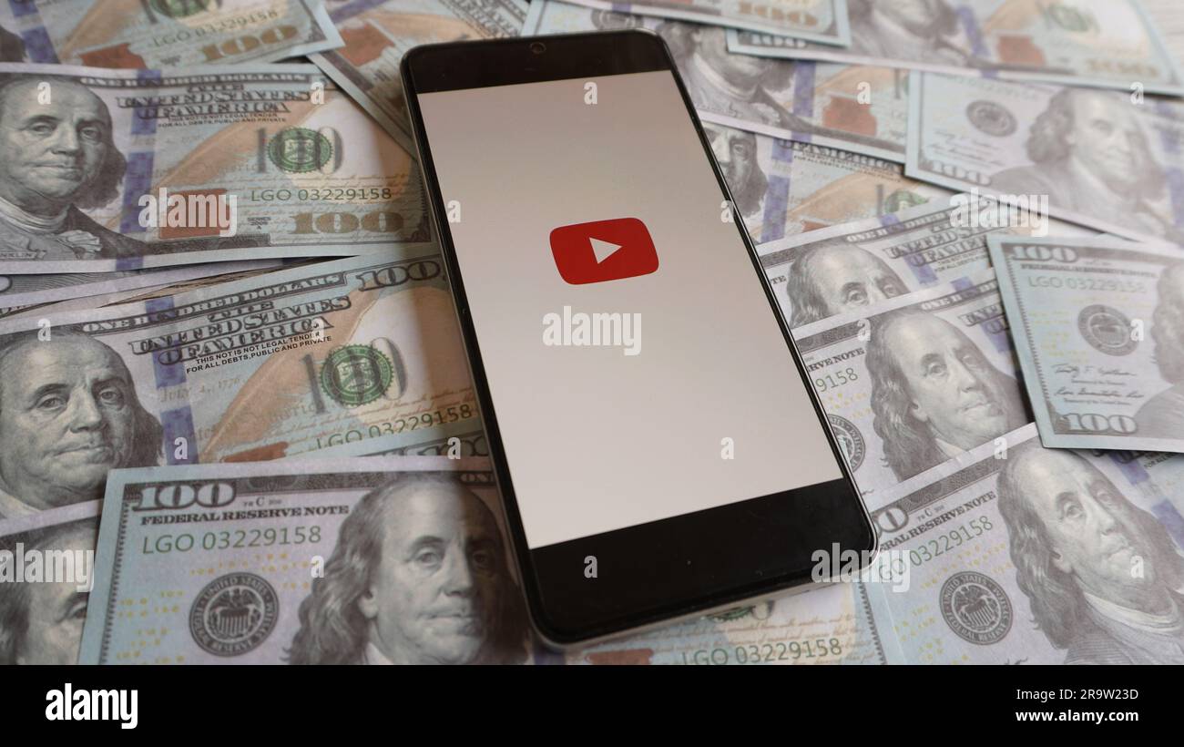 Logo YouTube su smartphone e stack di denaro. Monetizzazione del canale, contenuti video e concetto di profitto Foto Stock