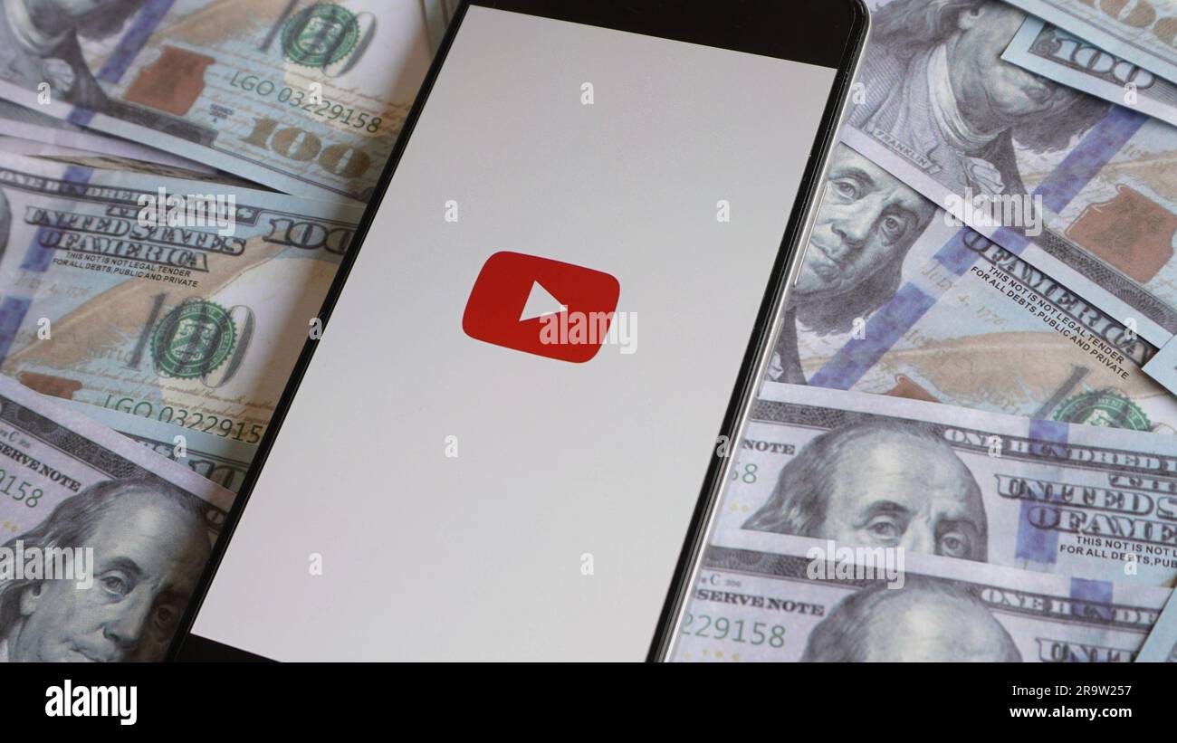 Logo YouTube su smartphone e stack di denaro. Monetizzazione del canale, contenuti video e concetto di profitto Foto Stock