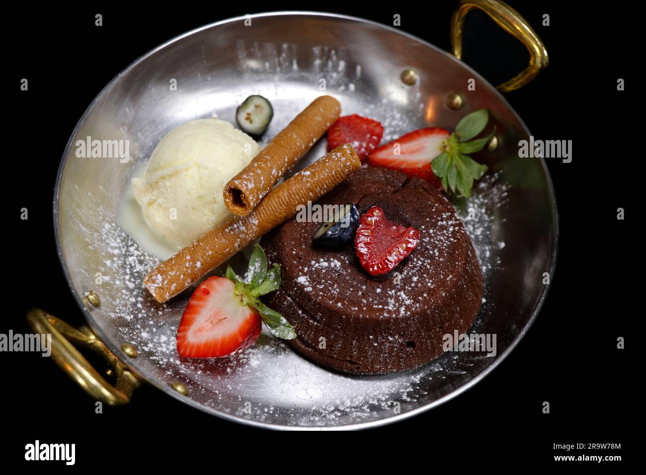 fondente al cioccolato al forno (torta di lava) con gelato alla vaniglia e frutti di bosco freschi assortiti, piatto di rame con fondo nero Foto Stock