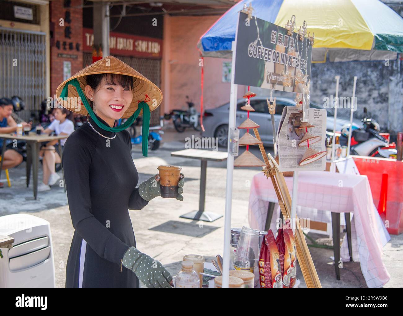 Febbraio 25 2023- George Town -Penang-Malesia-bellissima giovane donna malese con cappello specifico e vestito di nero vende caffè ai turisti smi Foto Stock