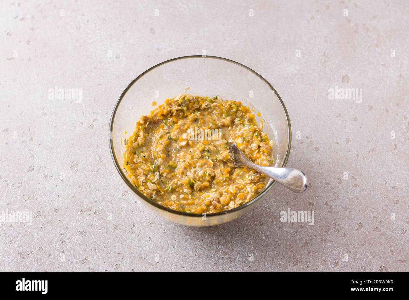 Recipiente di vetro con impasto per muffin alla zucca con farina d'avena, noci e cannella su uno sfondo ruvido beige. Cucinare deliziosi pasticcini autunnali fatti in casa. Foto Stock