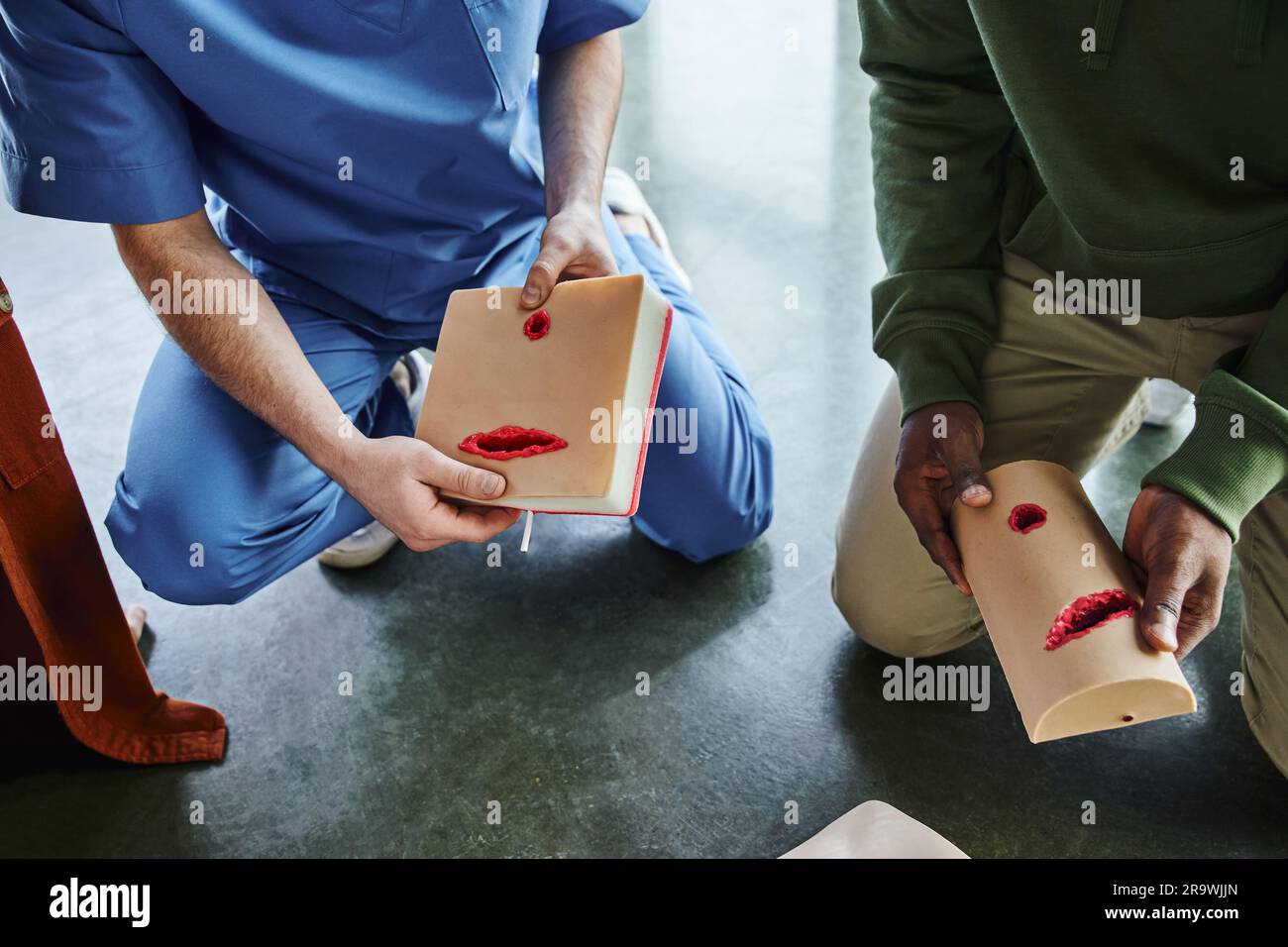 vista parziale dell'uomo afro-americano e istruttore medico professionista che tiene simulatori di cura delle ferite durante l'apprendimento pratico nella sala di formazione, cassaforte Foto Stock