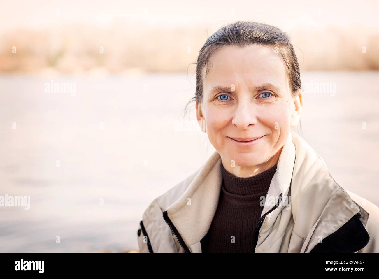Un caldo ritratto di un bel sorriso donna senior vicino al fiume Foto Stock