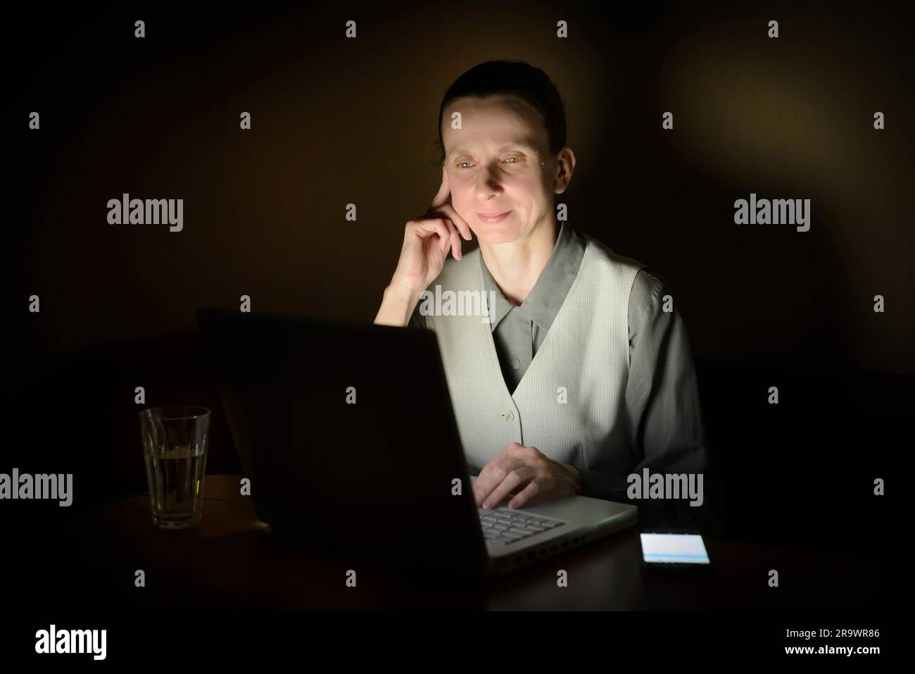 Una donna d'affari sta usando un computer in una stanza buia. Il suo volto è illuminato dalla luce del monitor lcd Foto Stock