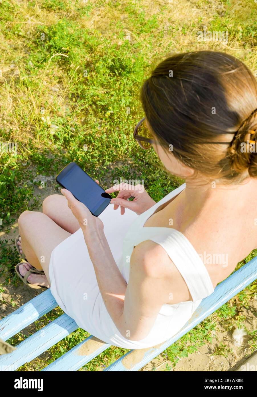 Un senior donna si siede su una panchina woden e utilizzato uno smartphone per inviare un messaggio di testo Foto Stock
