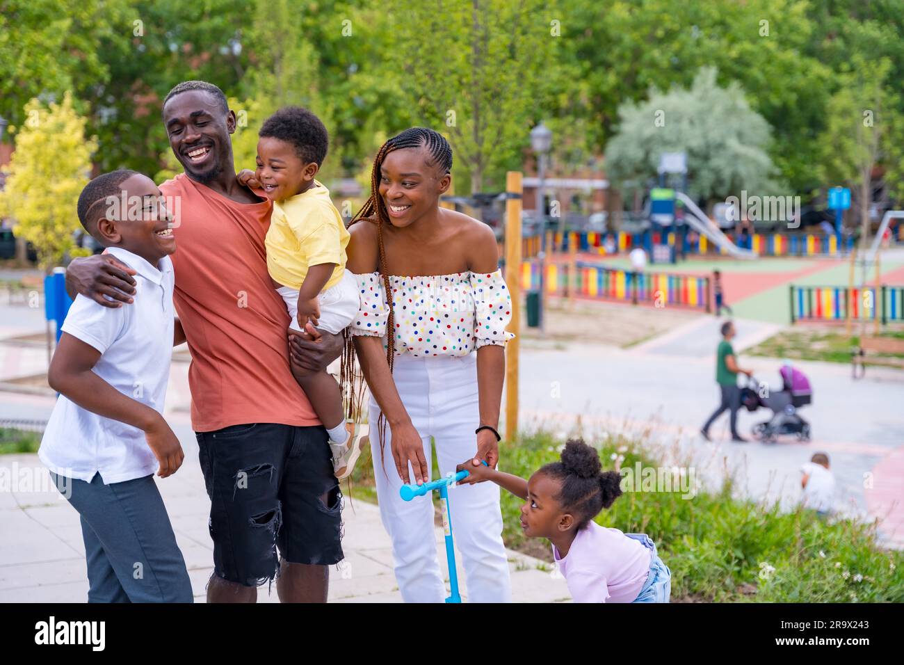 Famiglia di etnia nera africana che si diverte con i bambini felici insieme nel parco giochi, salutandosi a vicenda dopo la scuola Foto Stock