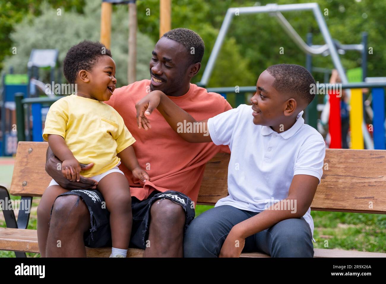 Padre di etnia nera africana che si diverte con i suoi figli nel parco giochi della città Foto Stock