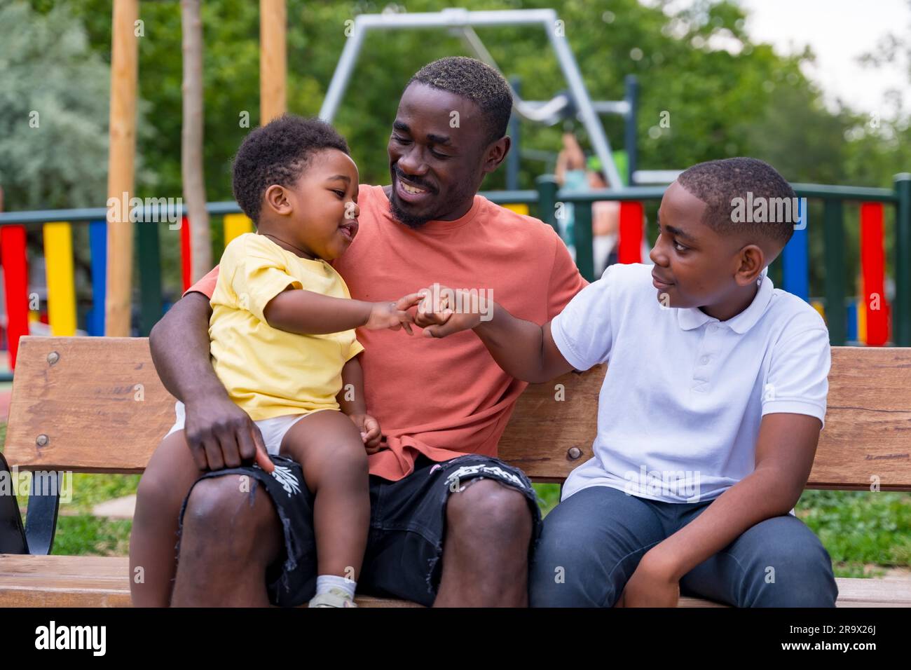 Padre di etnia nera africana che si diverte con i suoi figli nel parco giochi della città Foto Stock