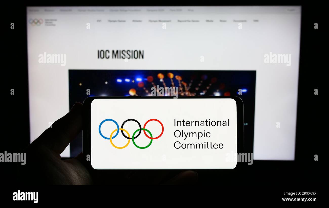 Persona che possiede uno smartphone con il logo del Comitato Olimpico Internazionale (CIO) sullo schermo di fronte al sito web. Concentrarsi sul display del telefono. Foto Stock