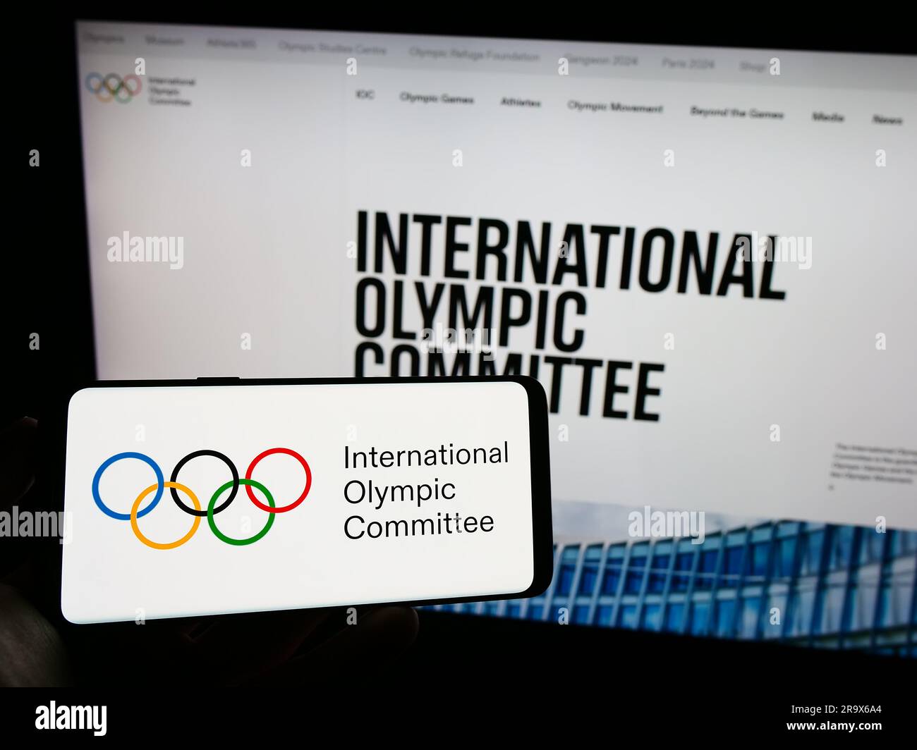 Persona che possiede un telefono cellulare con il logo del Comitato olimpico internazionale (CIO) sullo schermo davanti alla pagina web. Concentrarsi sul display del telefono. Foto Stock