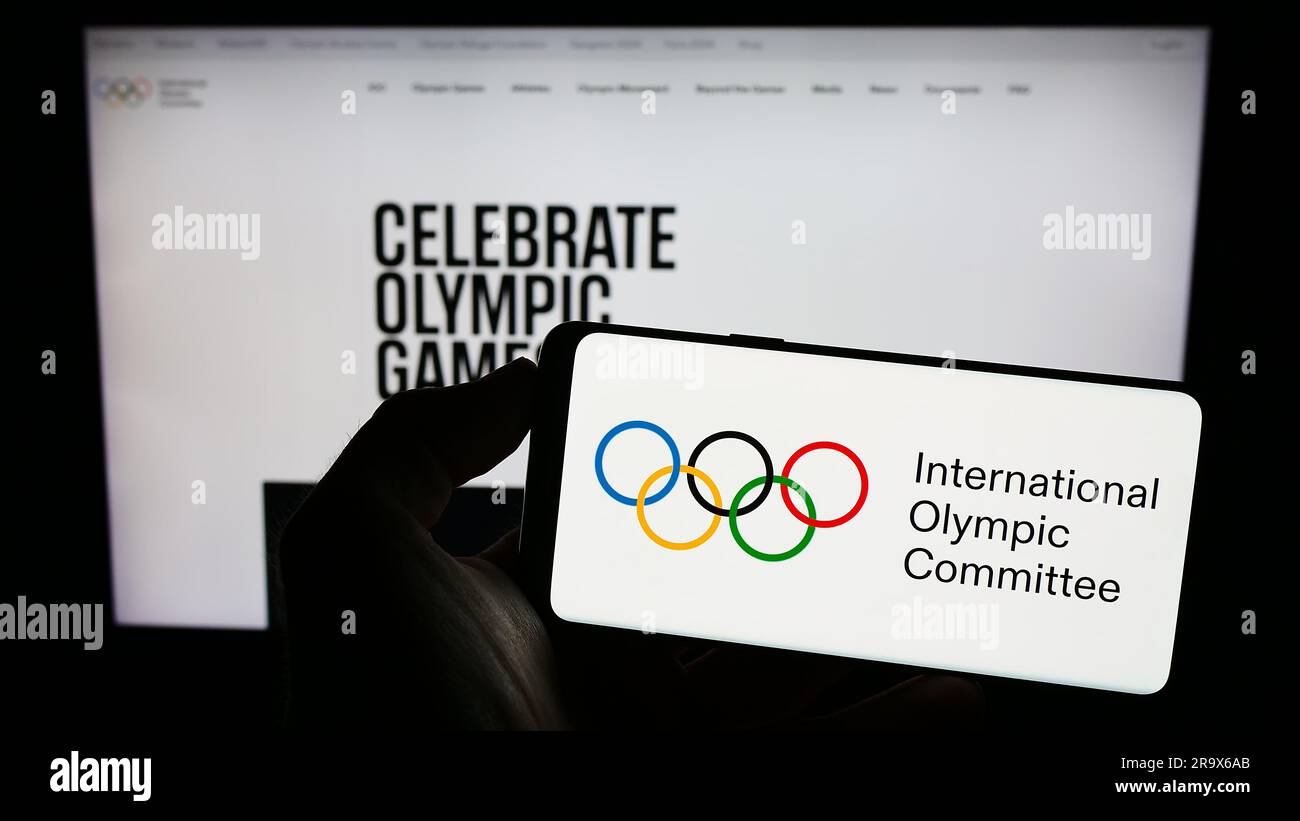 Persona in possesso di un cellulare con il logo del Comitato Olimpico Internazionale (CIO) sullo schermo davanti alla pagina web. Concentrarsi sul display del telefono. Foto Stock