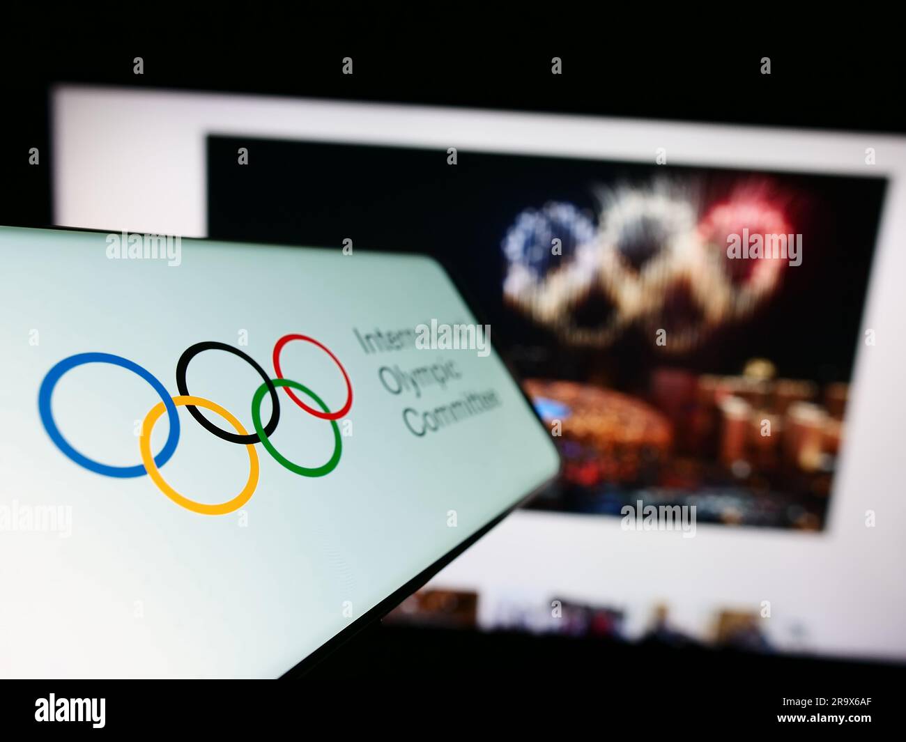 Telefono cellulare con logo del Comitato Olimpico Internazionale (CIO) sullo schermo davanti al sito web. Mettere a fuoco il display centrale sinistro del telefono. Foto Stock