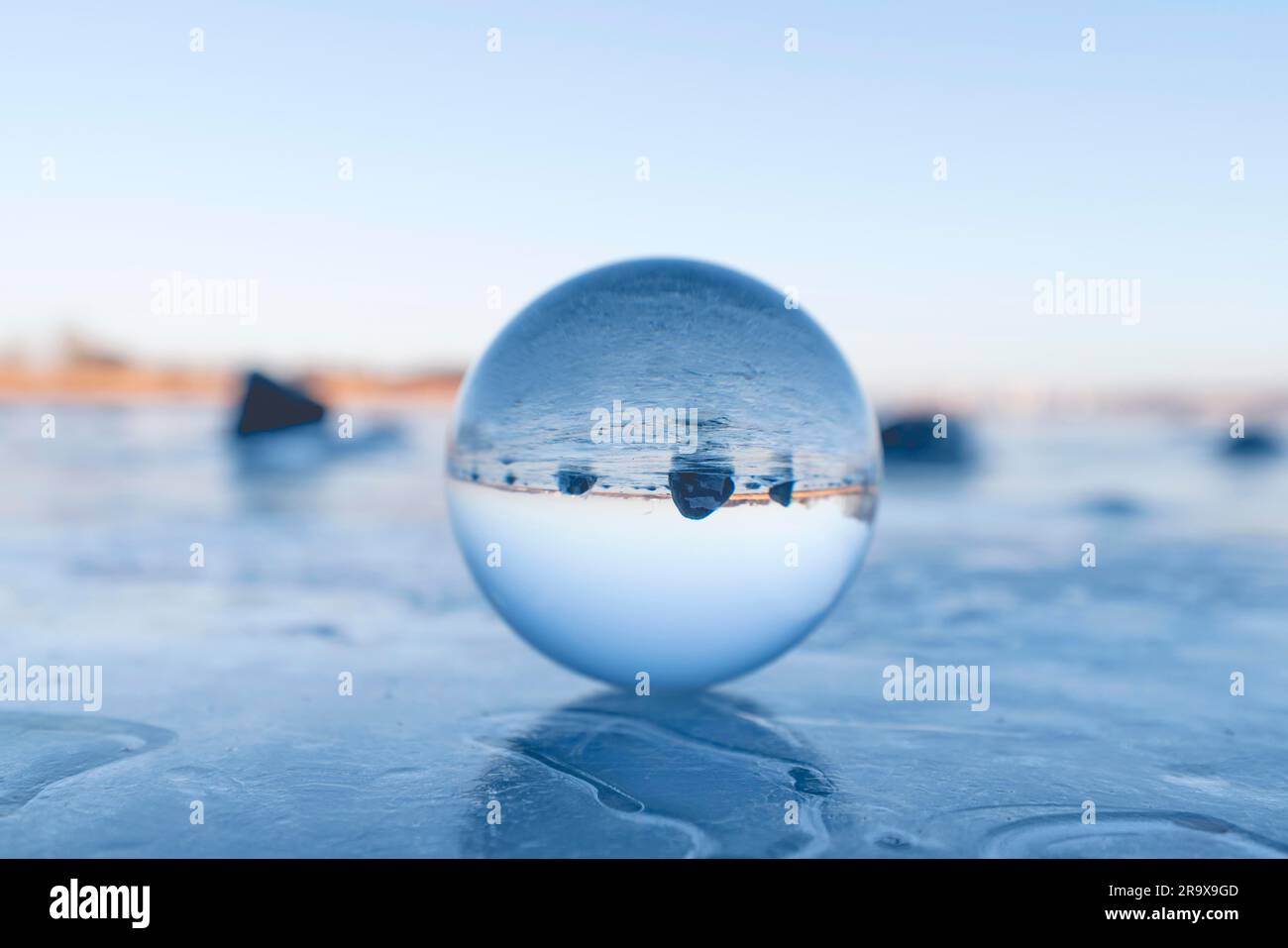 Sfera di cristallo su un lago ghiacciato in inverno con rocce nere in background Foto Stock