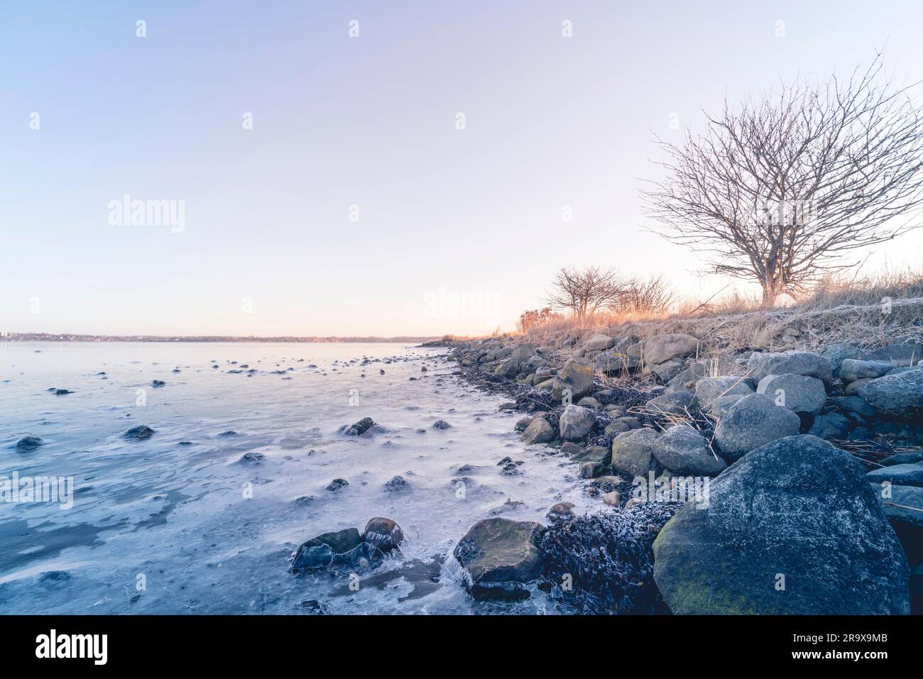Costa da un mare ghiacciato in inverno con rocce nel ghiaccio nella sunrise Foto Stock