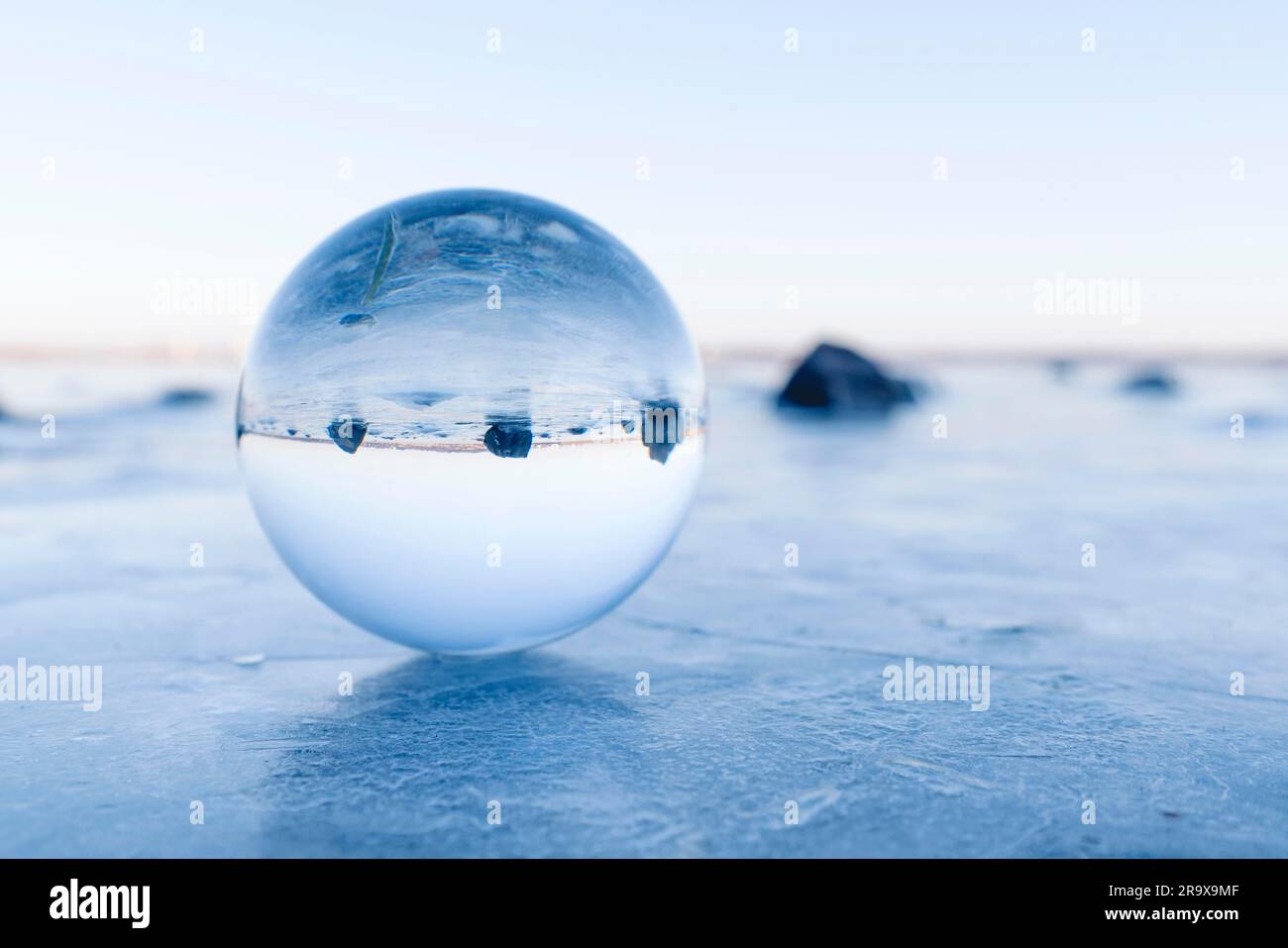 Rocce nere in una sfera di vetro su un lago ghiacciato in inverno Foto Stock