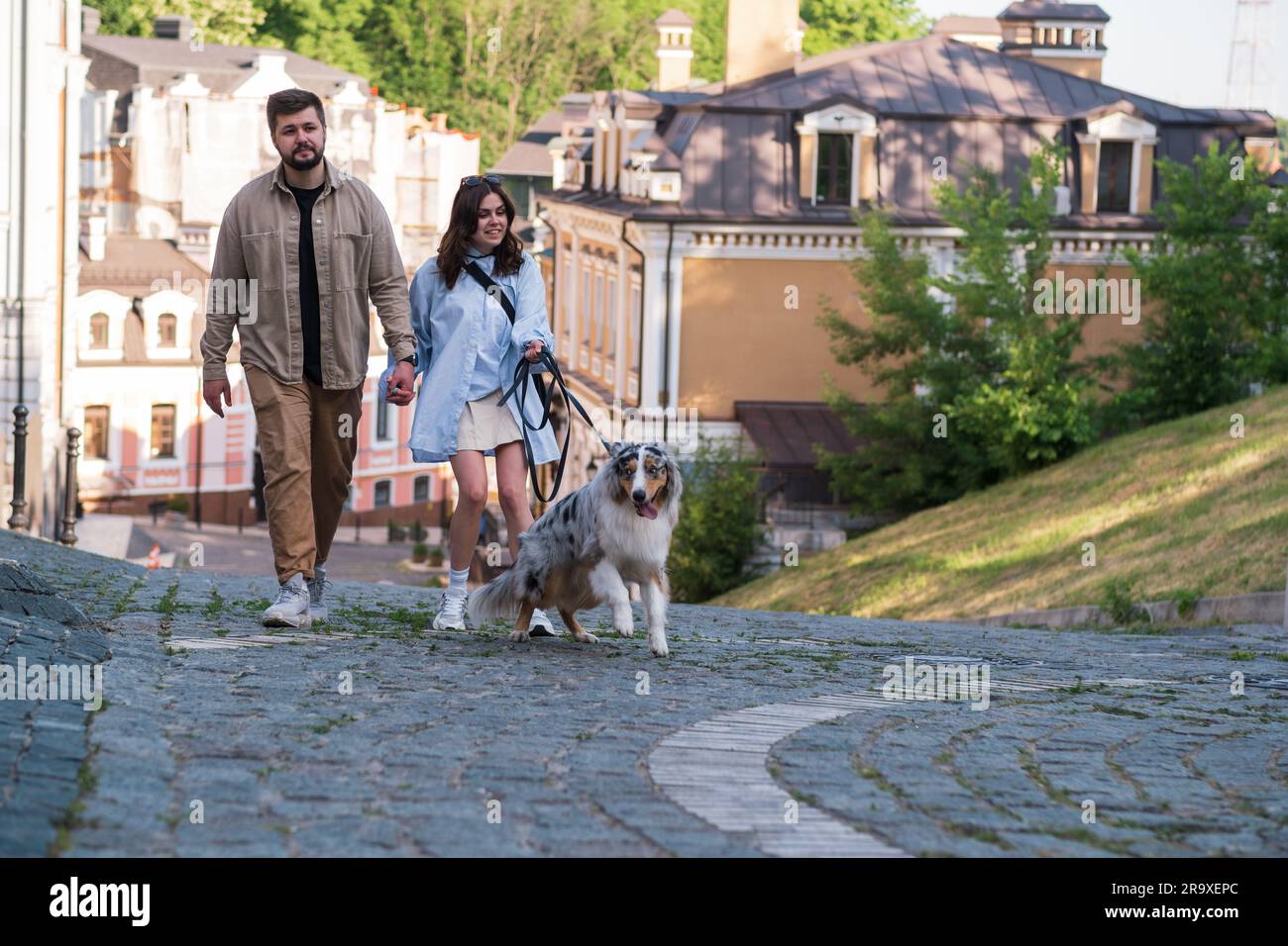 Uomo e donna che camminano con il loro cane australiano disobbediente fuori controllo, un momento divertente imbarazzante. Mal addestrato e comportato male giovane cane al guinzaglio Foto Stock