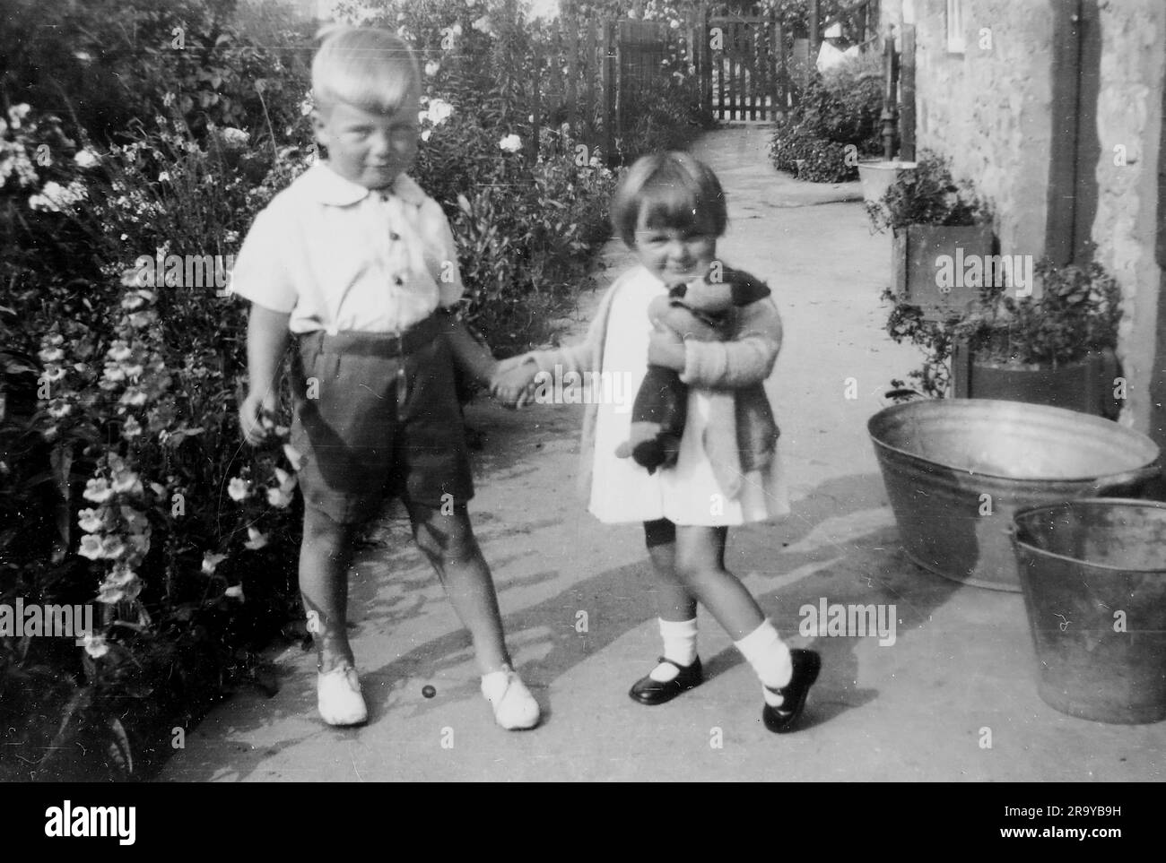 Un ragazzo e una ragazza in un giardino che si tengono per mano, la ragazza che stringe un orsacchiotto, Surrey, c1930. Si tratta di una fotografia tratta da un album di scatti, durante l'occupazione della Palestina da parte dell'esercito britannico, con foto provenienti dalla Palestina e dal Regno Unito, tra cui devil's Jump vicino a Churt nel Surrey e devil's Punch Bowl. L'addestramento sembra essere a Hursley Camp, vicino a Winchester. La Gran Bretagna amministrò la Palestina per conto della società delle Nazioni tra il 1920 e il 1948, un periodo denominato "mandato britannico”. Foto Stock