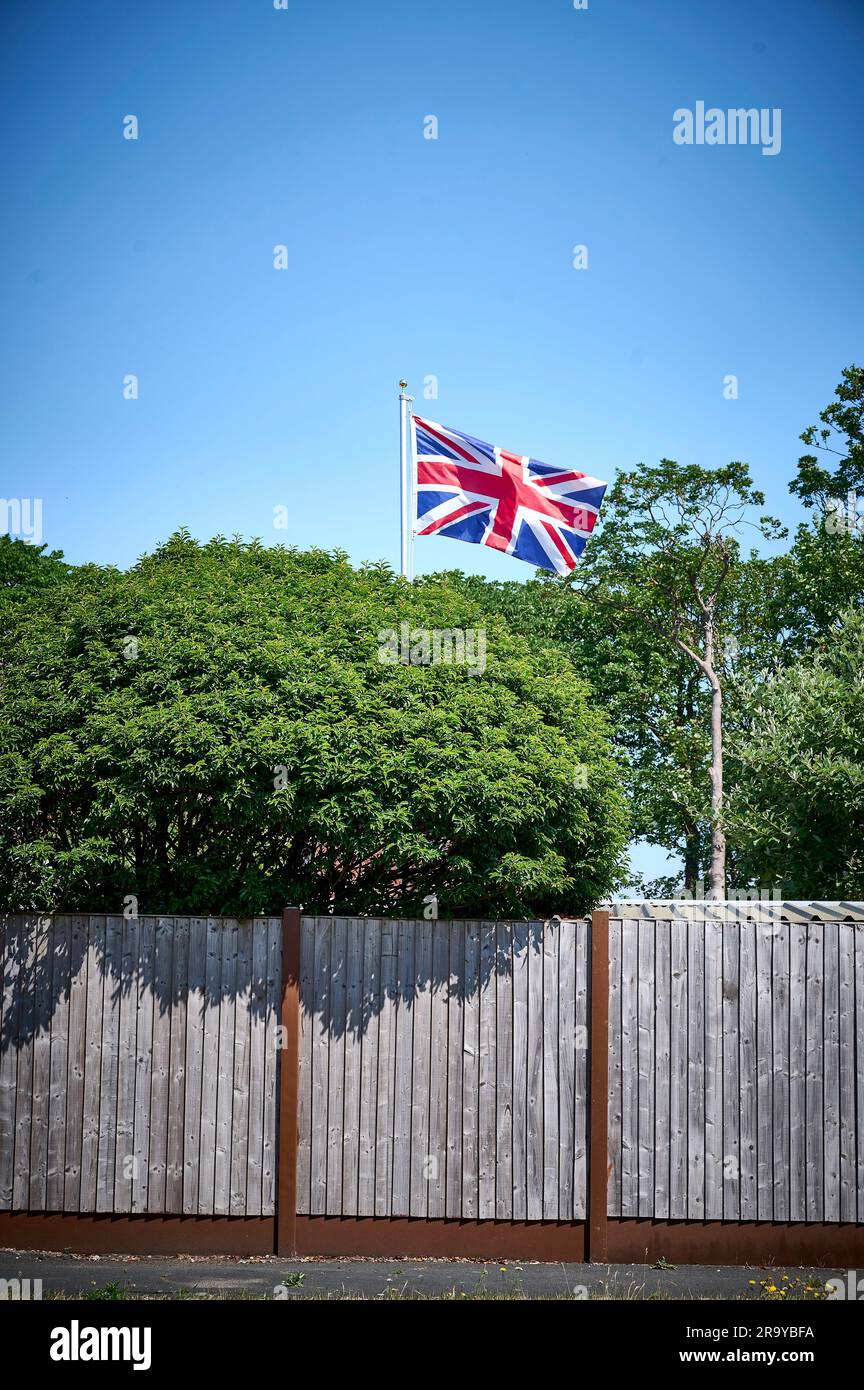 Union Jack su palo da bandiera che vola sopra la recinzione del giardino e gli alberi, St Annes, Regno Unito Foto Stock