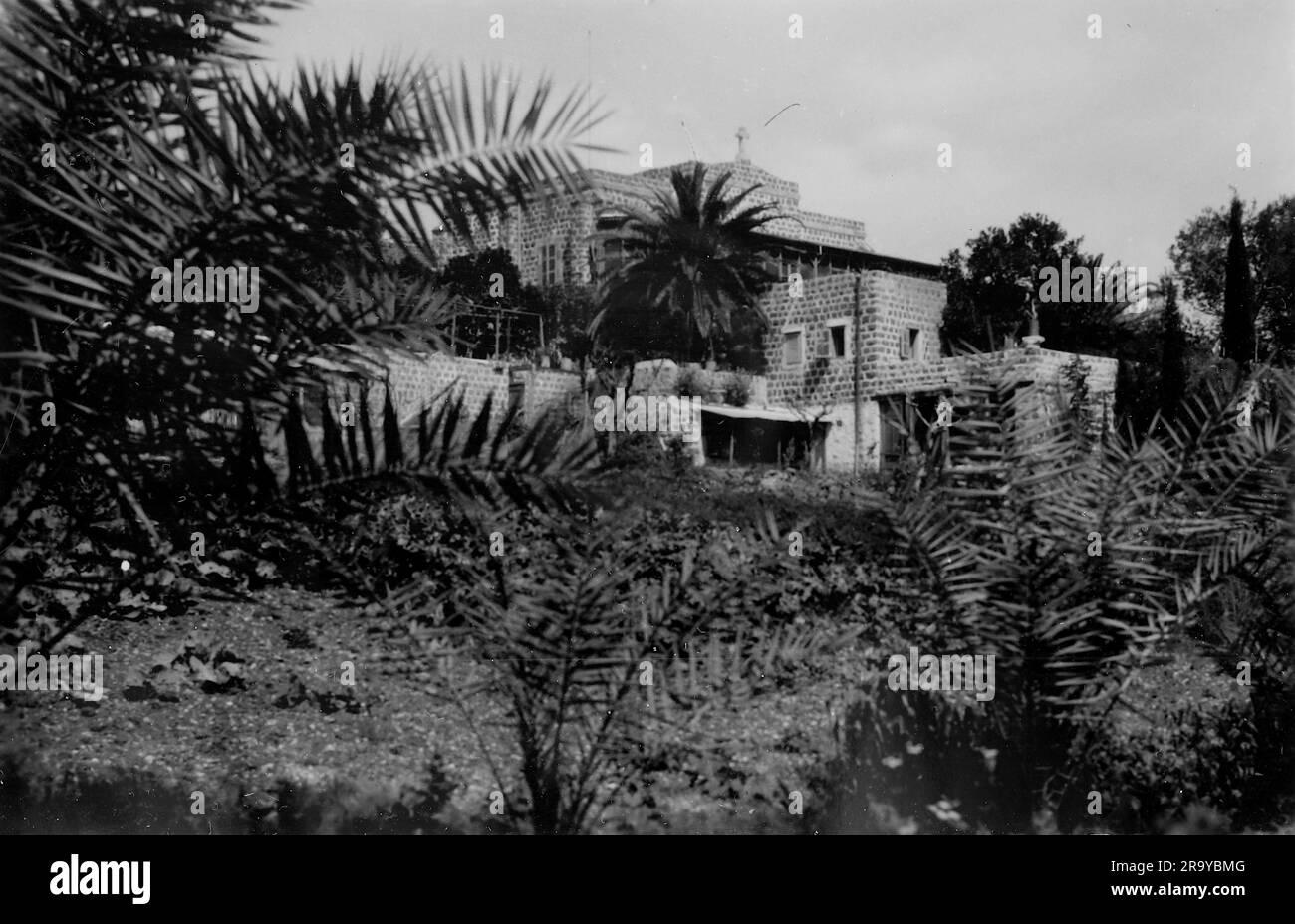 Una grande casa parzialmente nascosta dalla flora autoctona. Questa fotografia è tratta da un album fotografico di fotografie, c1937, durante l'occupazione della Palestina da parte dell'esercito britannico. La Gran Bretagna amministrò la Palestina per conto della società delle Nazioni tra il 1920 e il 1948, un periodo denominato "mandato britannico”. Foto Stock