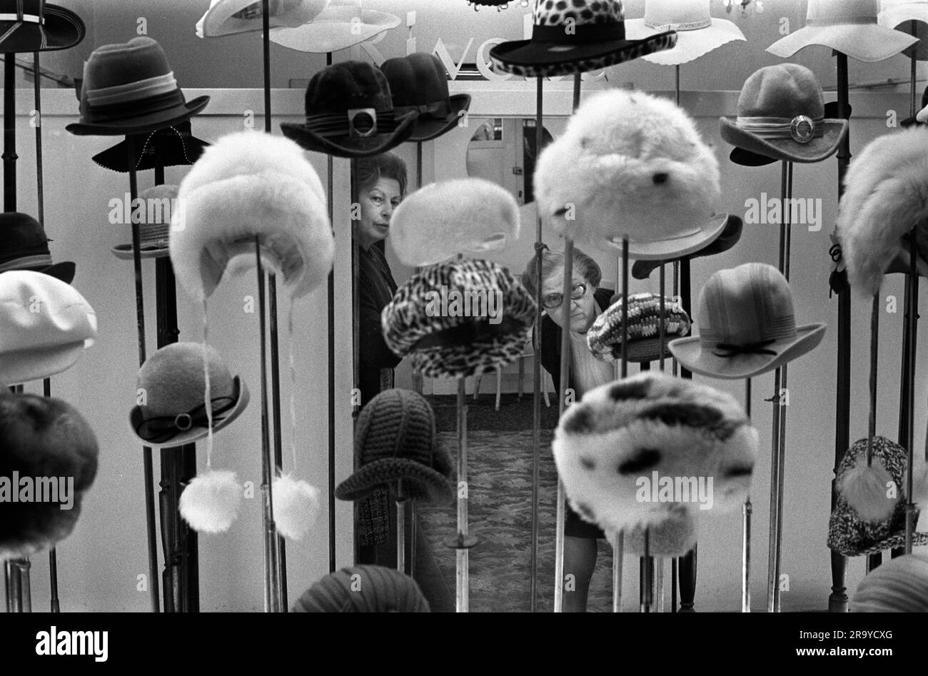 Vetrina,. Un elegante negozio di cappelli da donna e due assistenti da donna che guardano fuori. Mile End Road. Tower Hamlets, Londra, Inghilterra circa 1974. 1970 UK HOMER SYKES Foto Stock